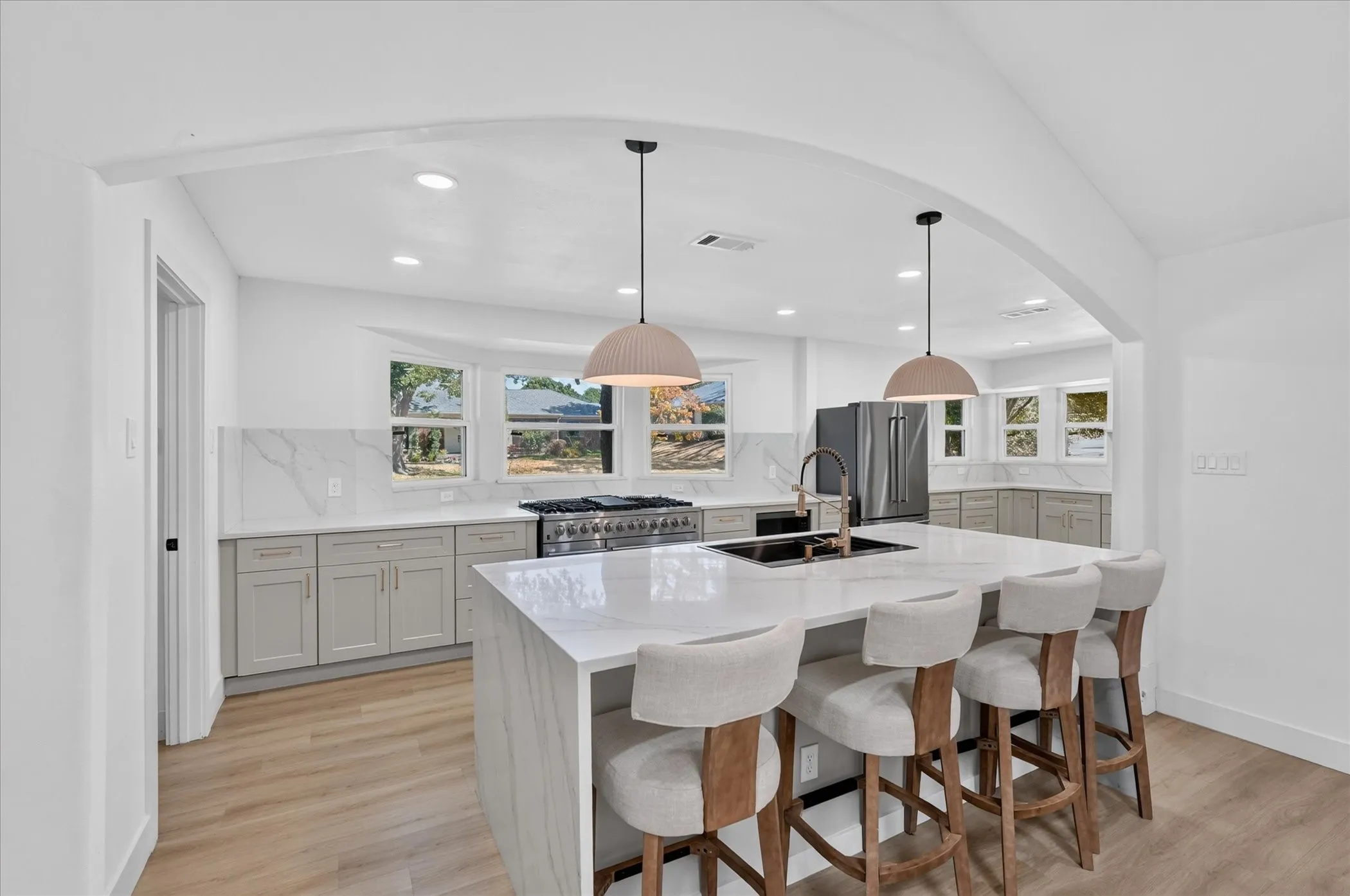 Expansive kitchen featuring a large central island with waterfall countertop, recessed lighting, wood-finish flooring, full range with hood, and stainless steel refrigerator