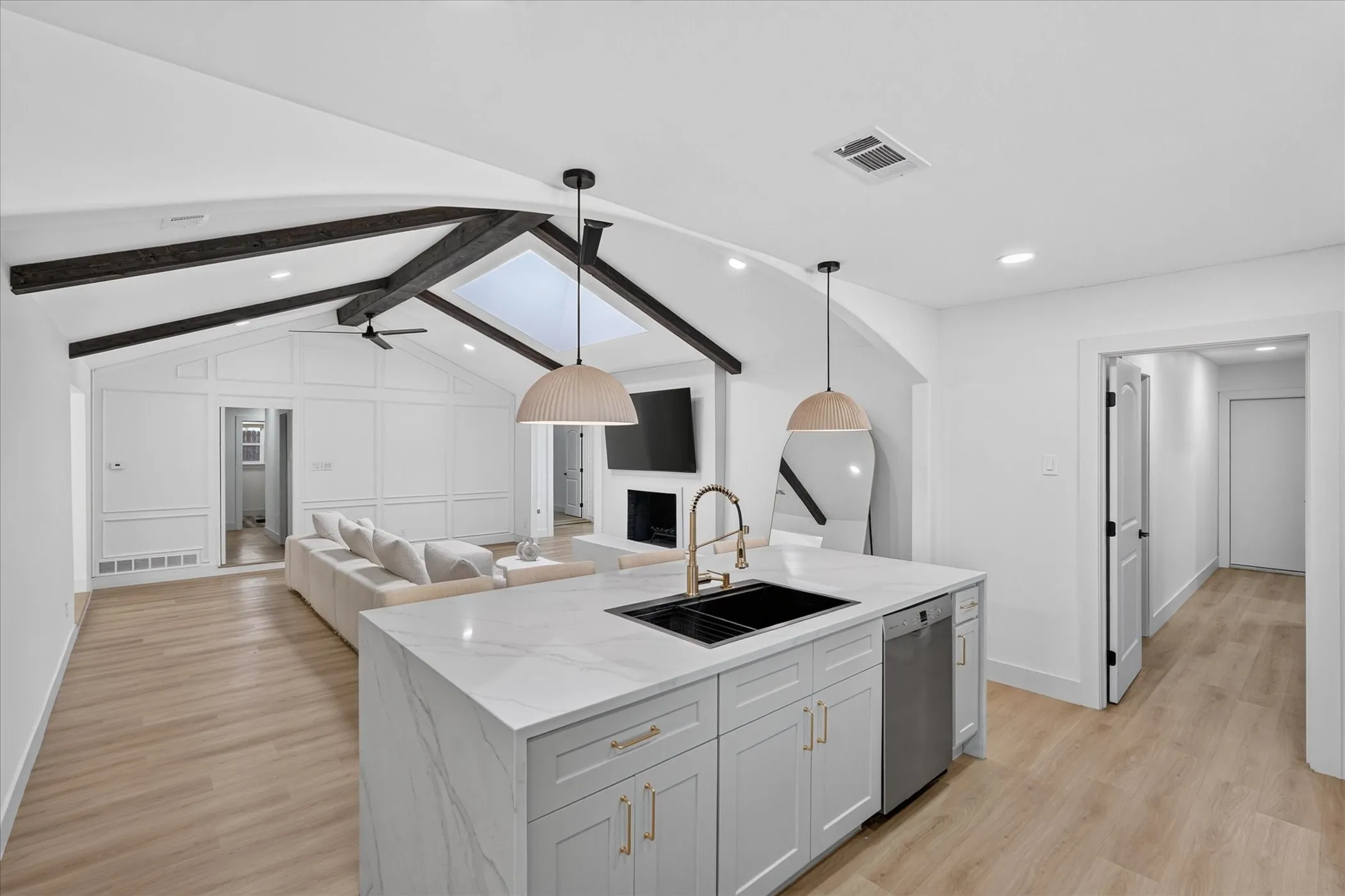 Kitchen island with integrated sink, wood-finish flooring, vaulted ceiling with exposed beams, skylight, and recessed lighting