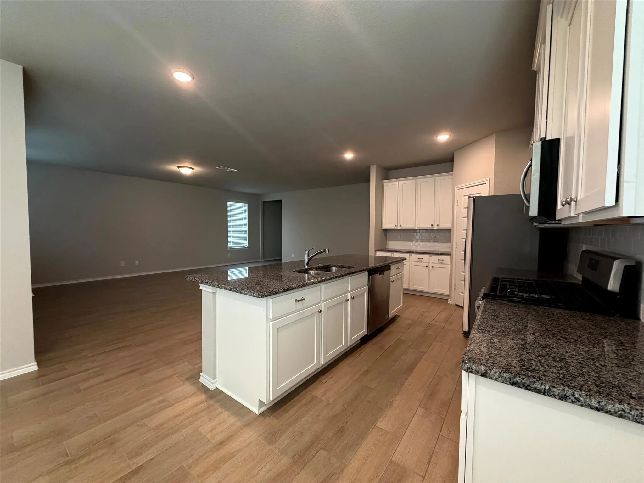 Open-concept kitchen featuring an island with undermount sink, granite countertops, white cabinetry, and wood-finish flooring