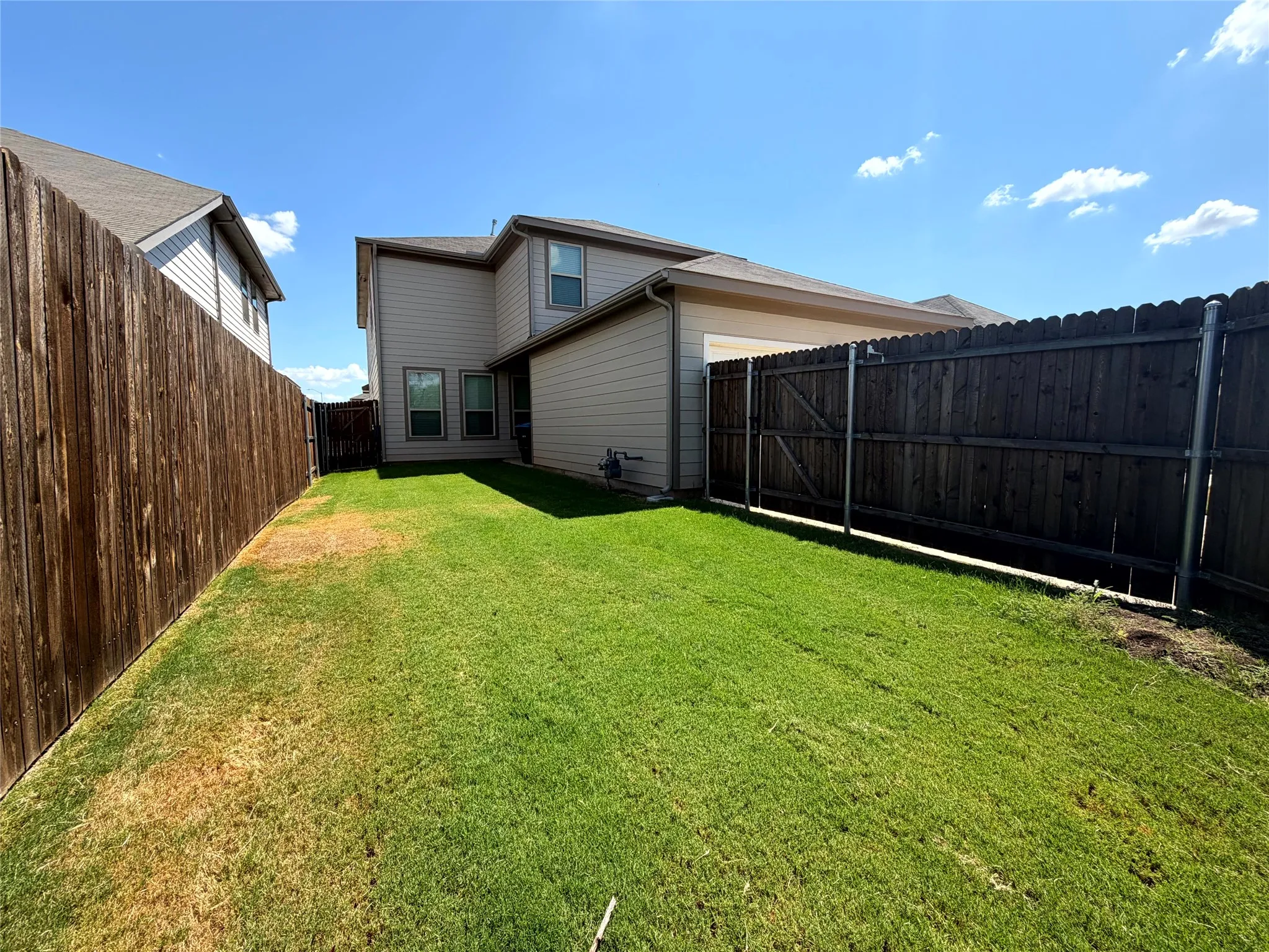 Expansive backyard featuring a privacy fence, manicured lawn, and multi-pane windows