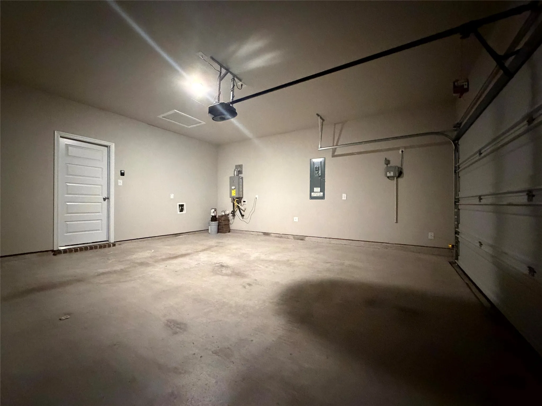 Attached garage with concrete flooring, a paneled interior door, overhead lighting, and an automatic garage door opener