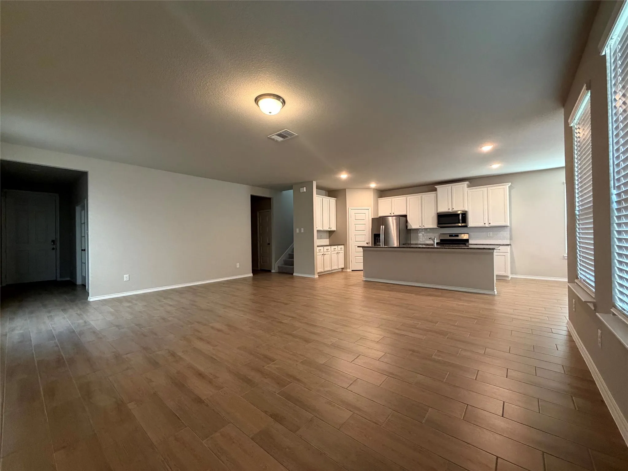 Open-concept living space featuring wood-finish flooring, recessed lighting, white cabinetry, a kitchen island, and stainless steel appliances