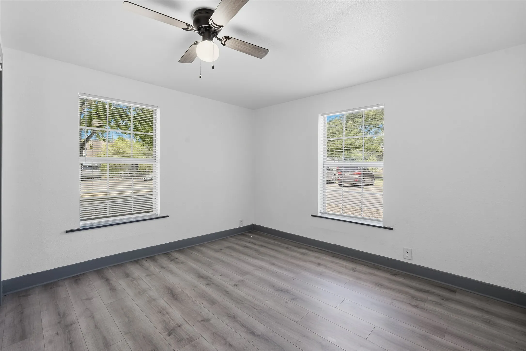 Bright interior space featuring wood-finish flooring, white walls, and two windows with blinds