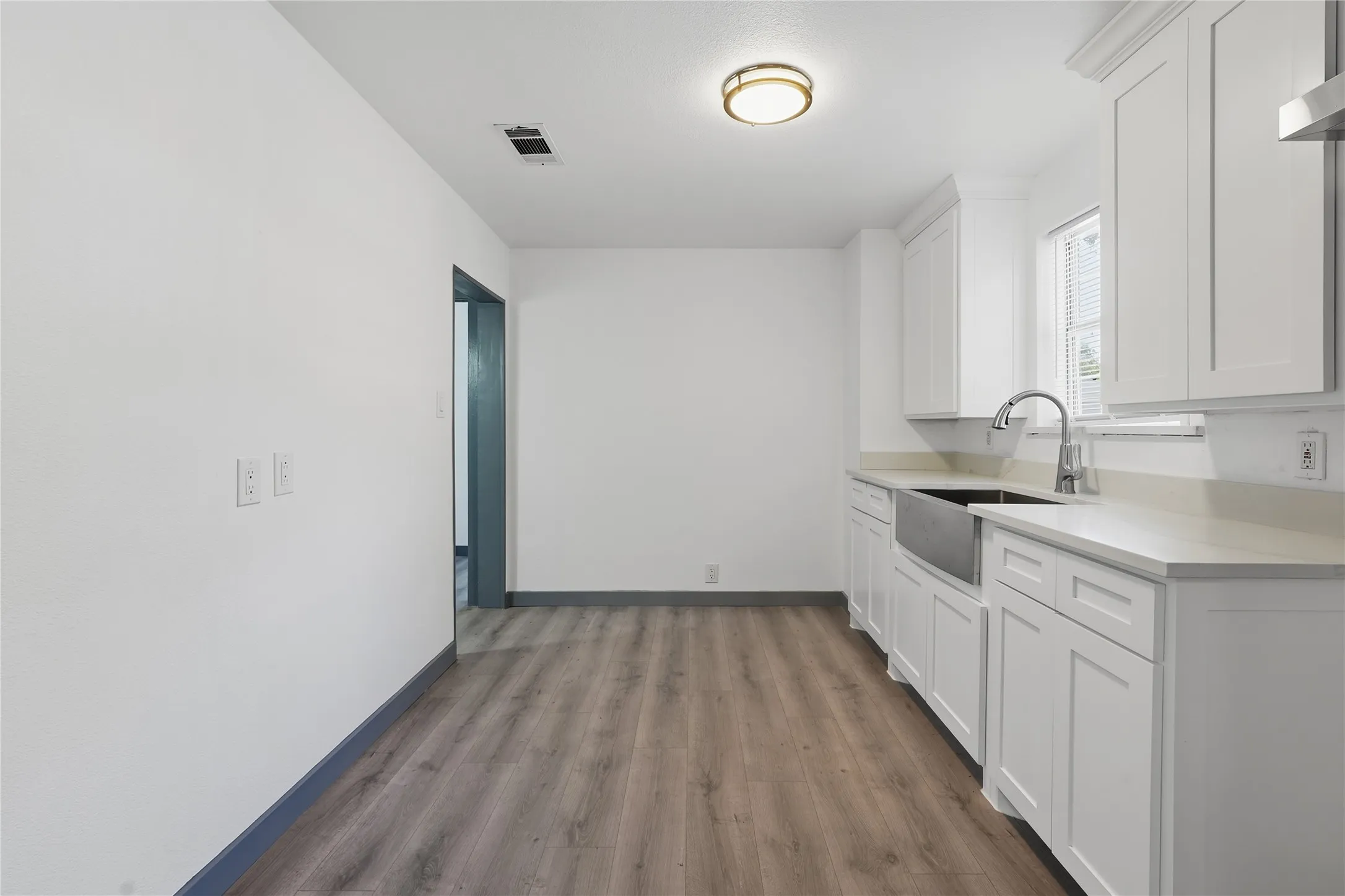 Contemporary kitchen with white shaker cabinetry, light-toned countertops, a stainless steel farmhouse sink, and wood-finish flooring