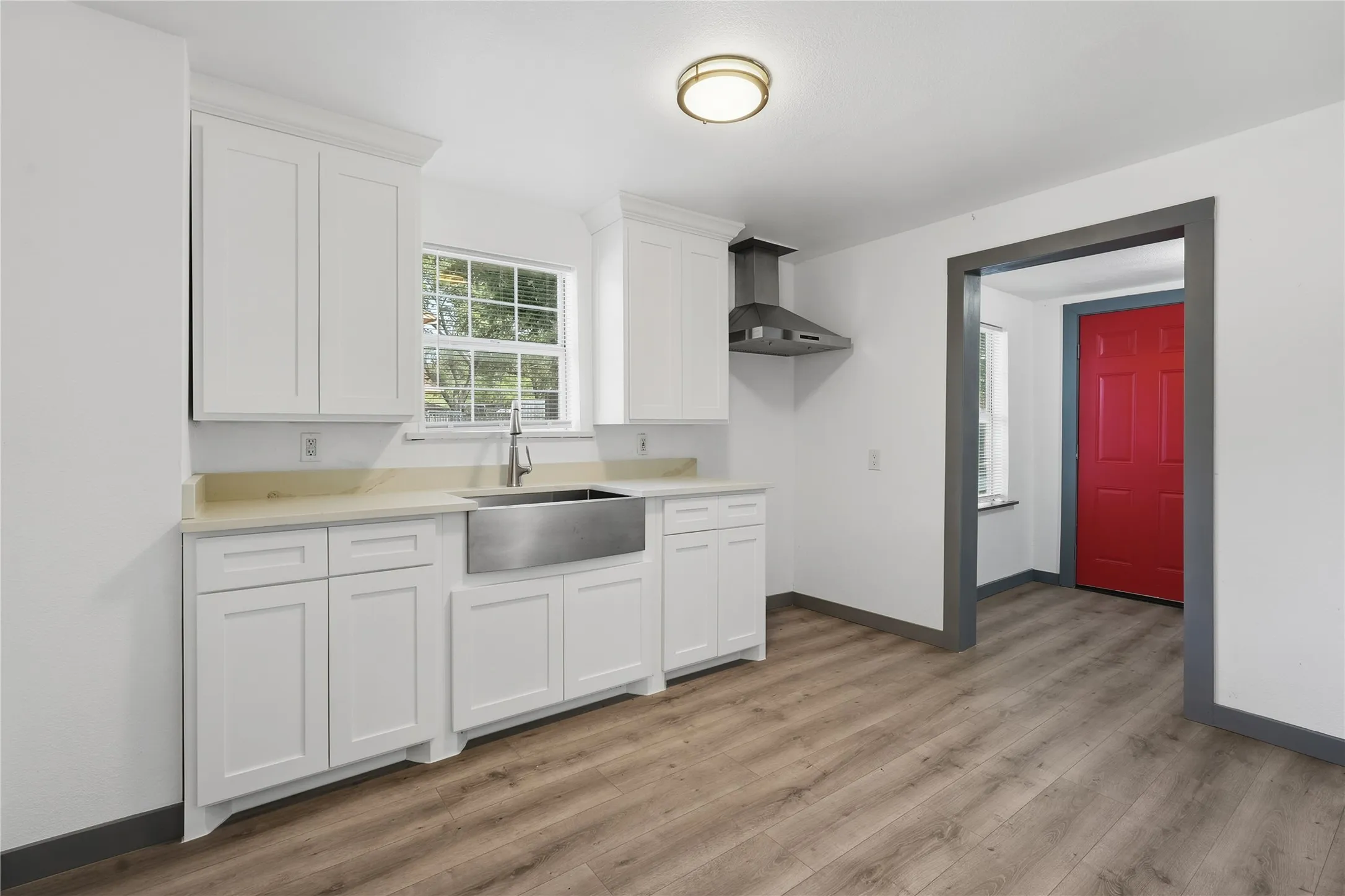White shaker cabinetry with crown molding, stainless steel farmhouse sink, modern range hood, wood-finish flooring, and a flush-mount ceiling light