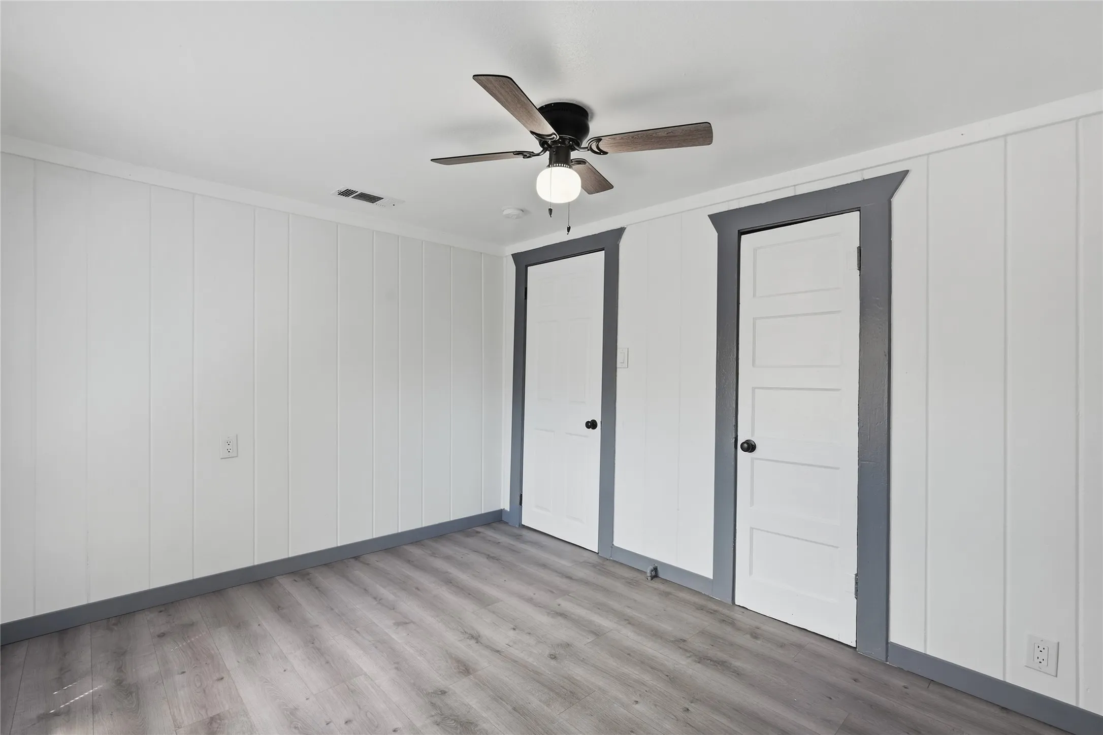 Wood-finish flooring, paneled walls, and a ceiling fan with integrated lighting