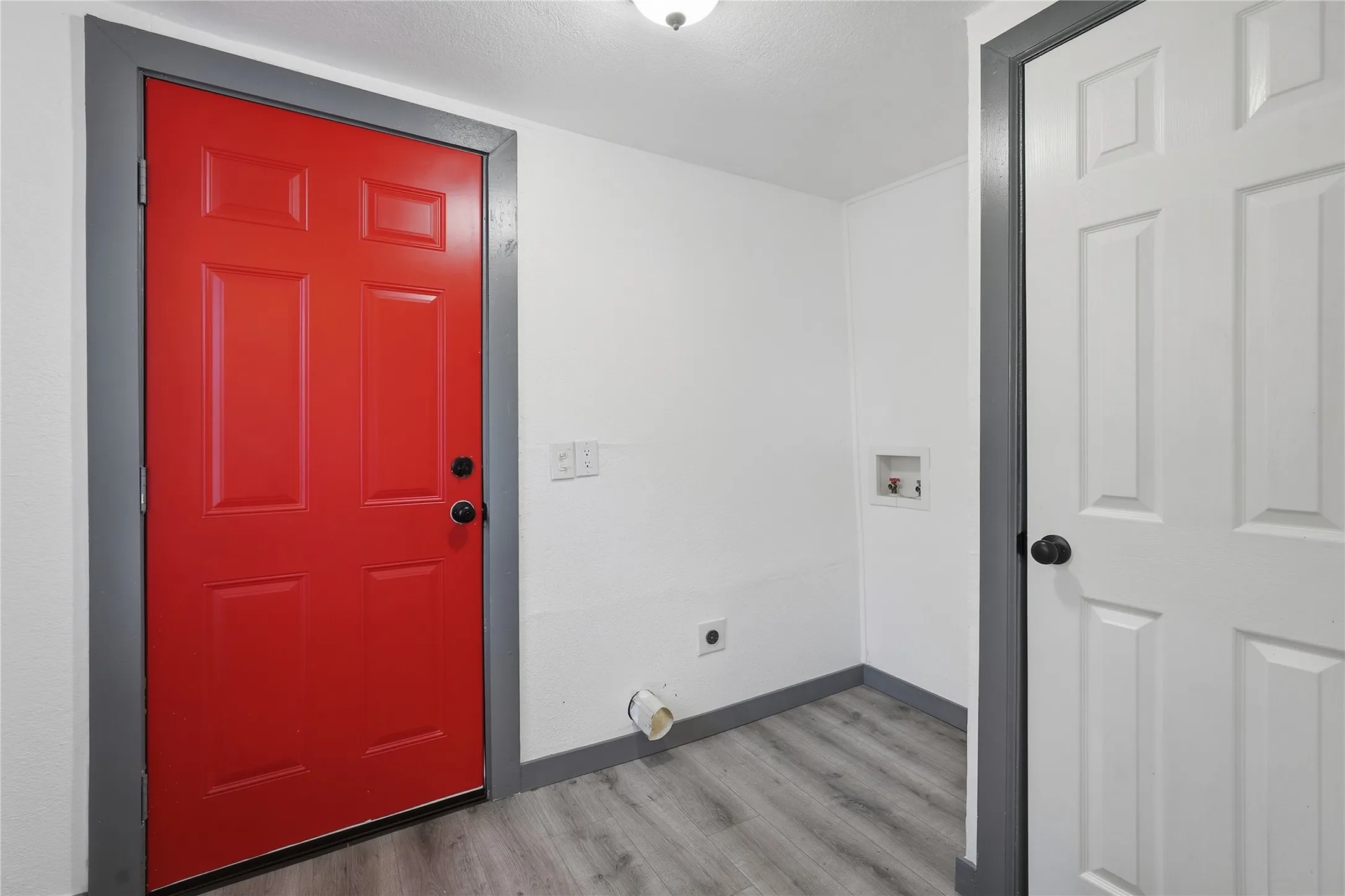 Vibrant red panel door with contrasting trim, wood-finish flooring, and utility hookups