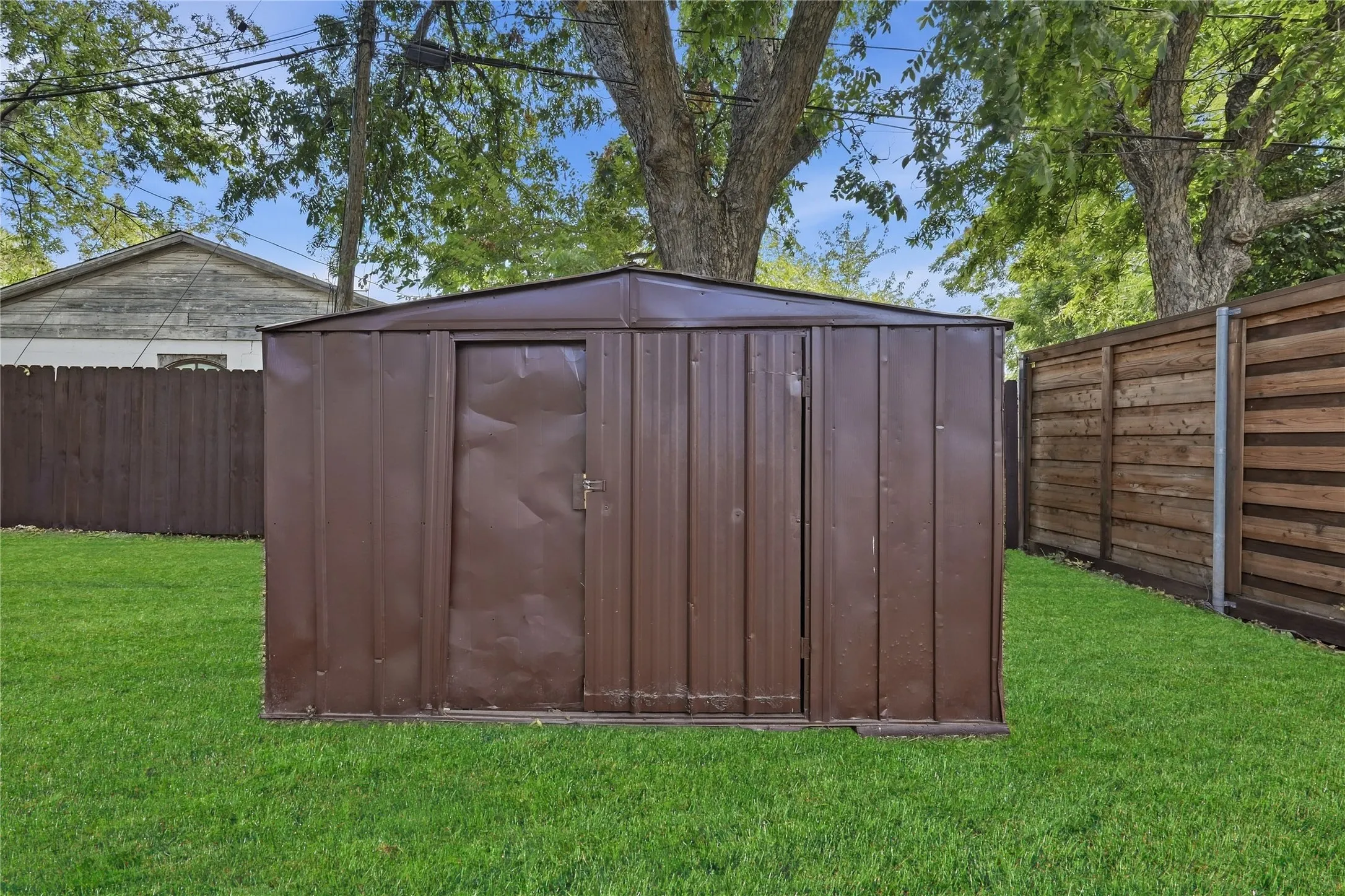 Manicured lawn with a brown metal storage shed and perimeter fencing
