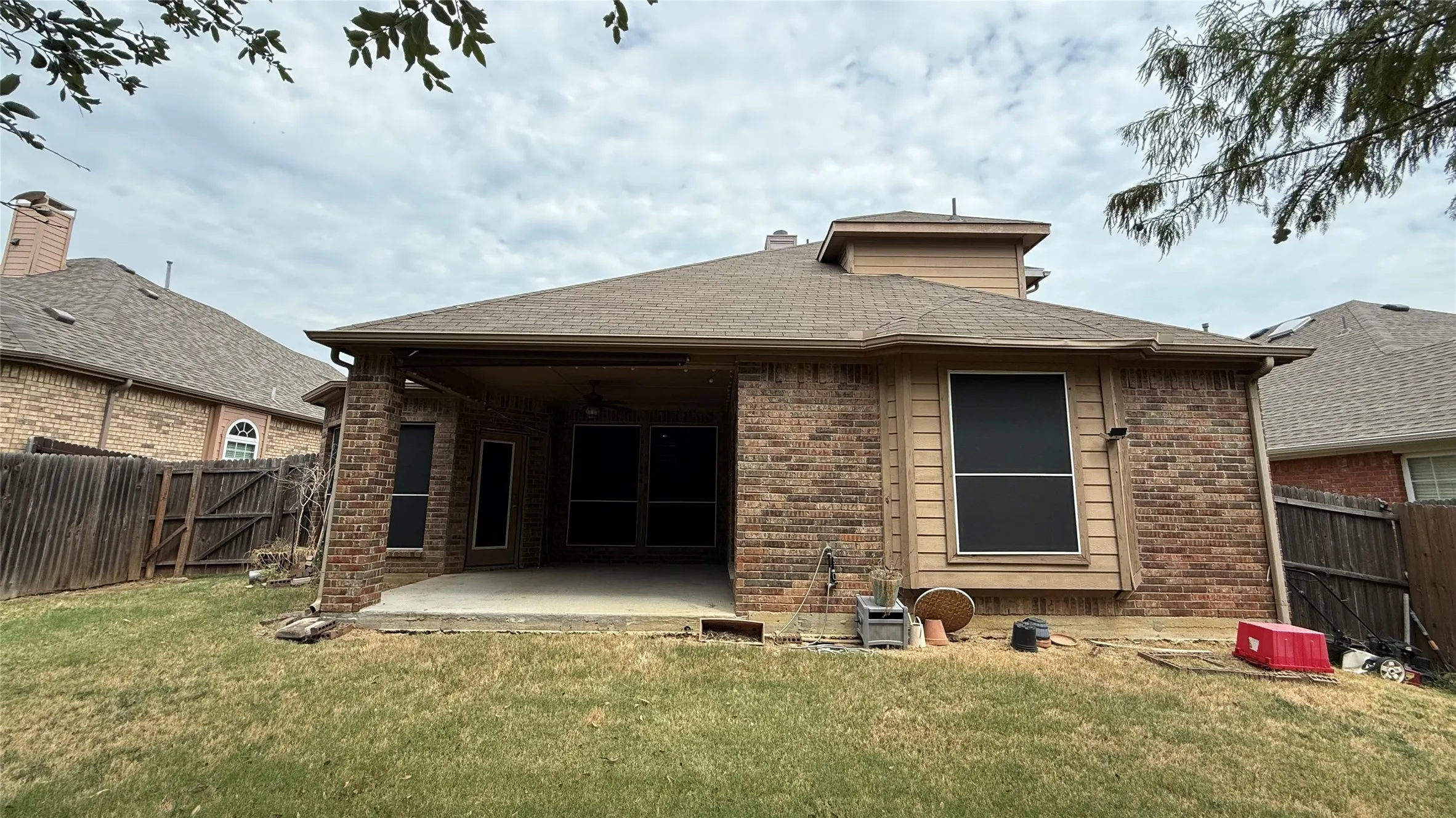 Brick exterior with covered patio, concrete patio surface, and shingle roof