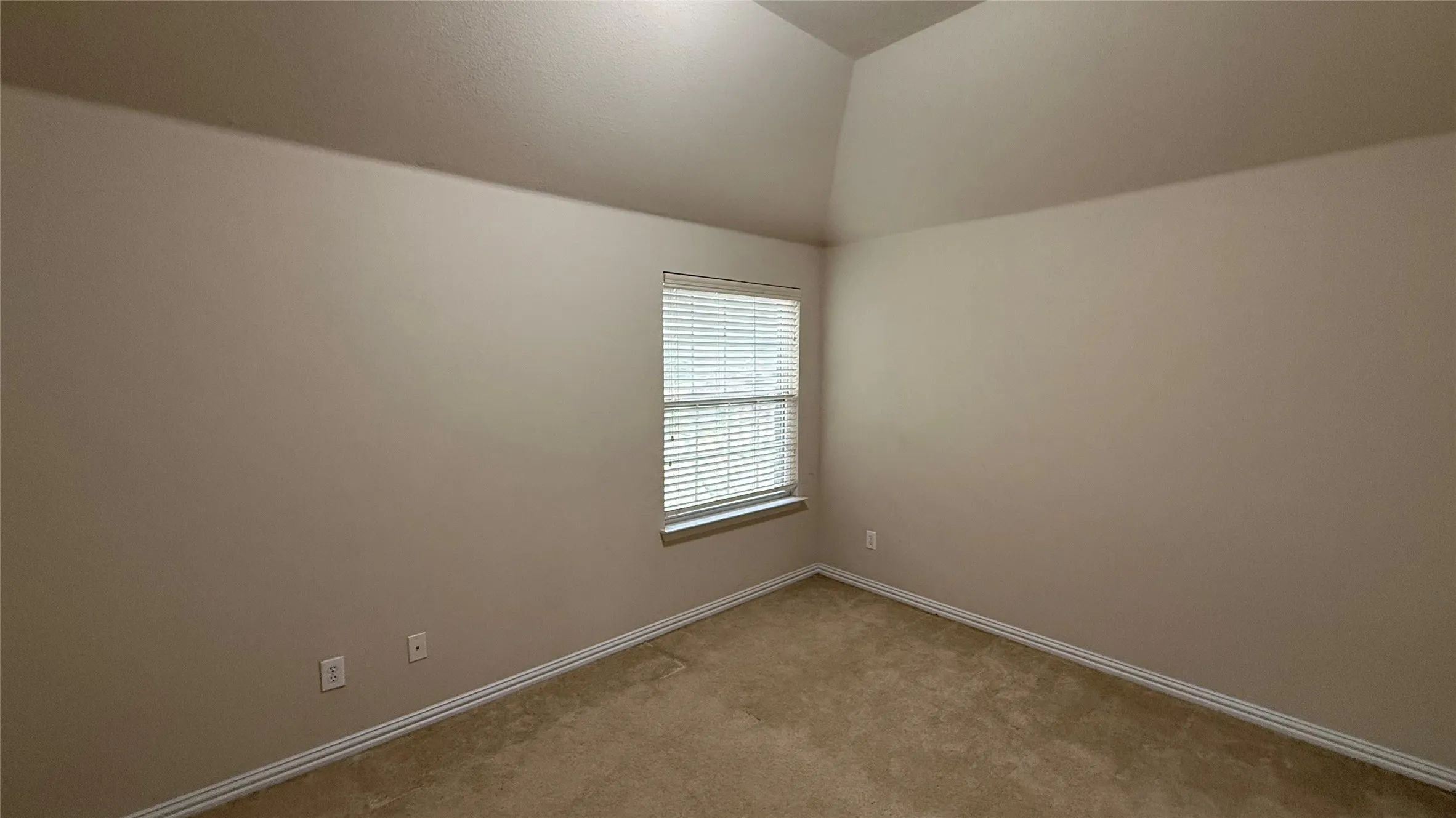 Vaulted ceiling with neutral paint, carpeted flooring, and a single window with blinds