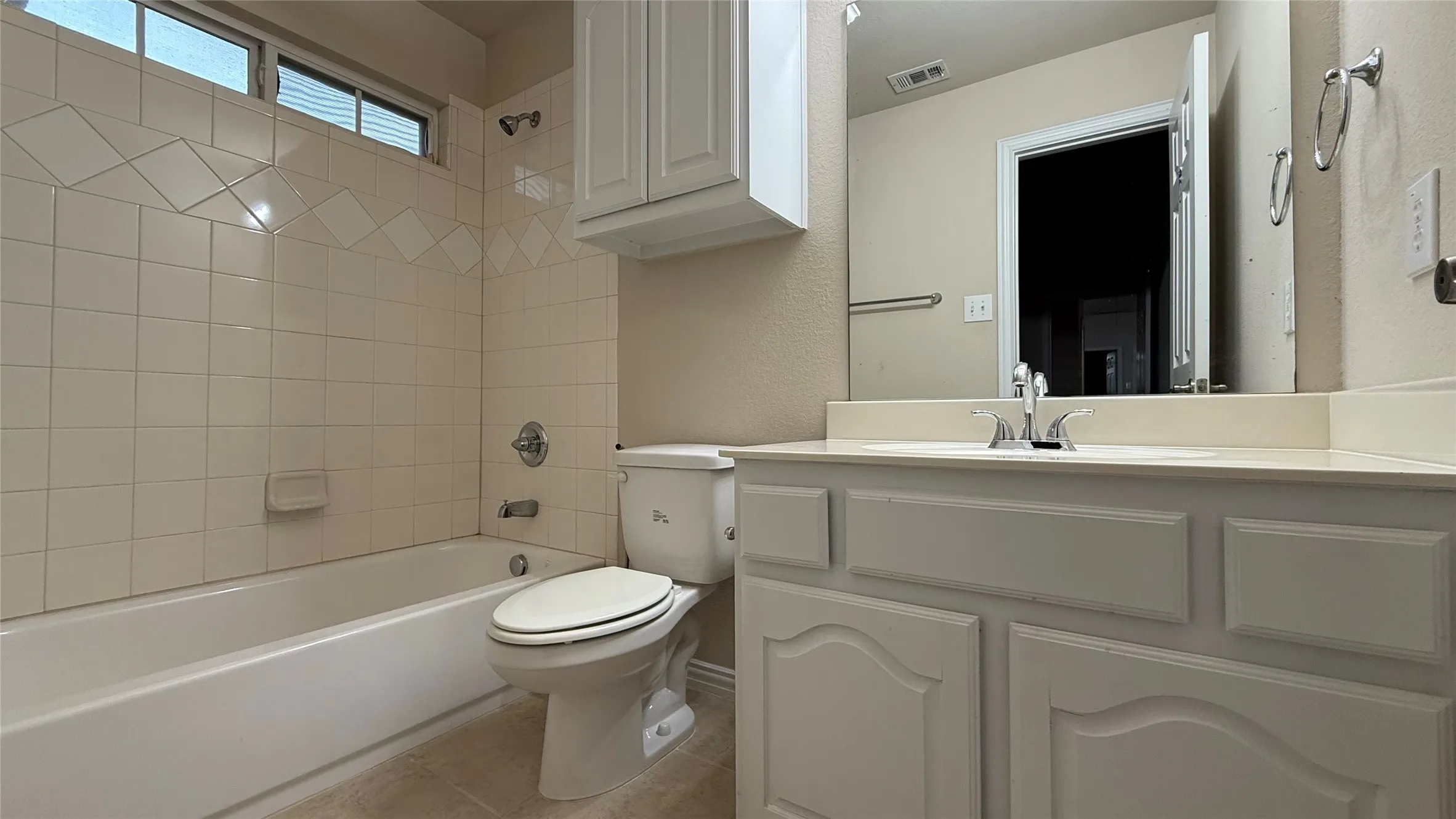 Bathroom featuring a built-in tub with tile surround, white vanity with integrated sink, and an overhead storage cabinet