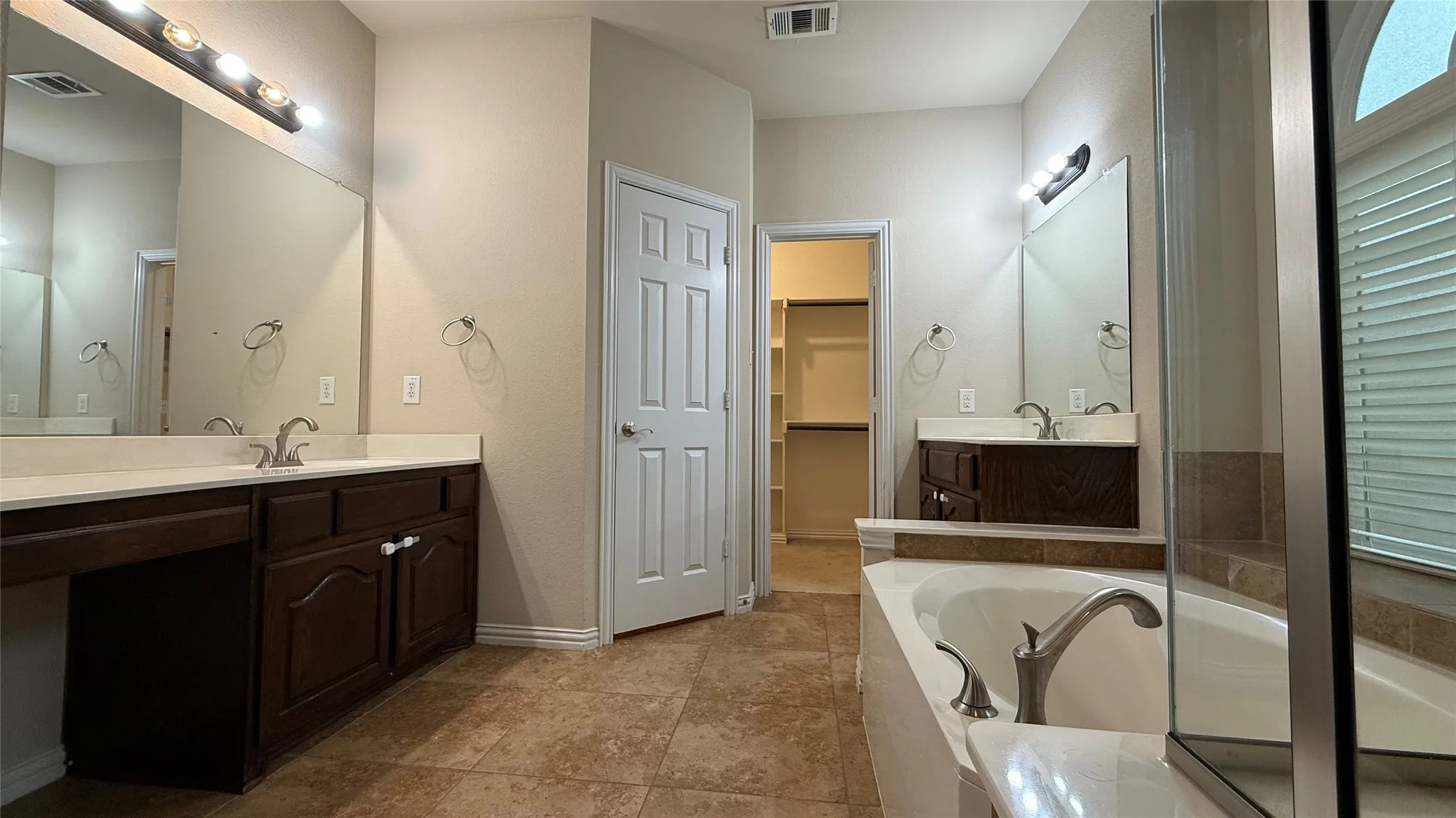 Dual vanity with white countertops, tiled flooring, built-in bathtub, and walk-in closet access