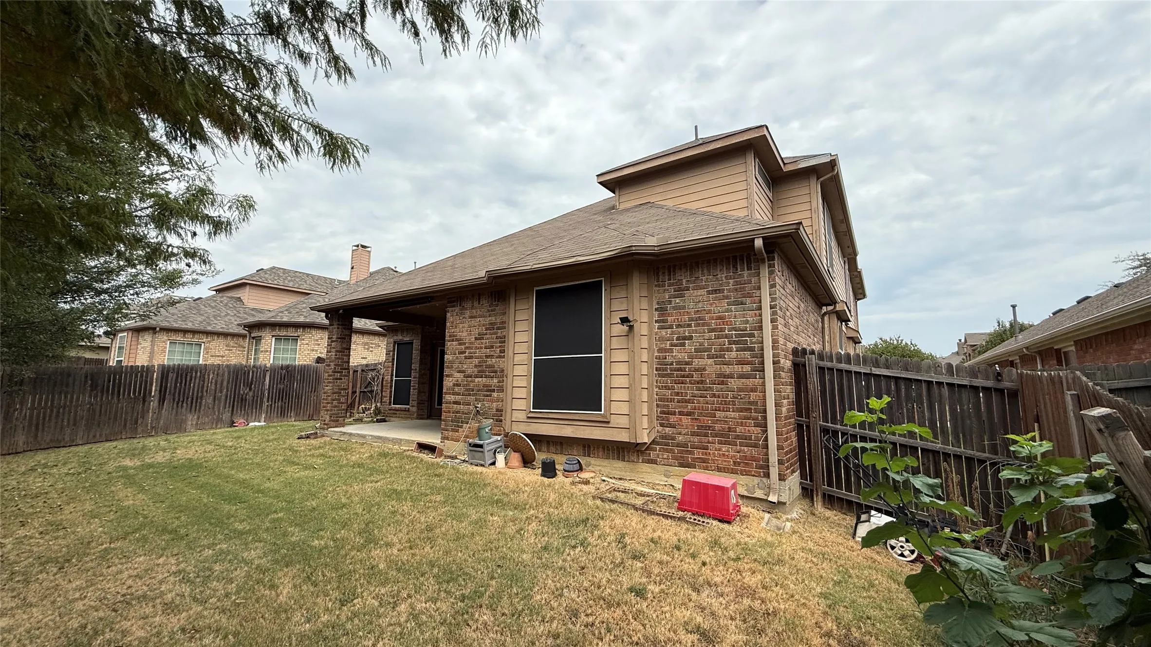 Brick and siding exterior with a covered patio, a privacy fence, and a sloped lawn