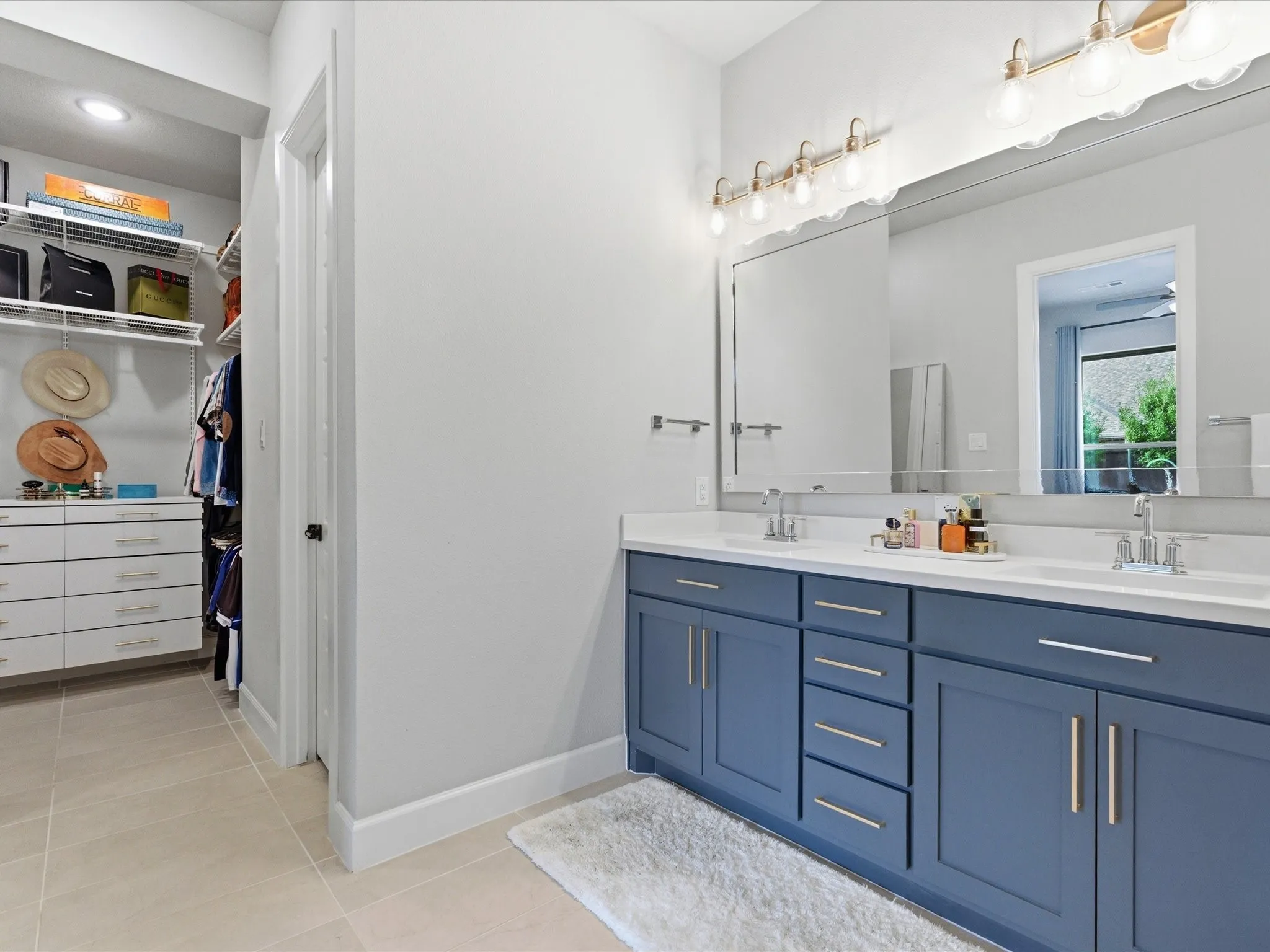 elegant bathroom featuring blue cabinetry, dual sinks, and with a glimpse into the spacious walk-in closet for added convenience and functionality