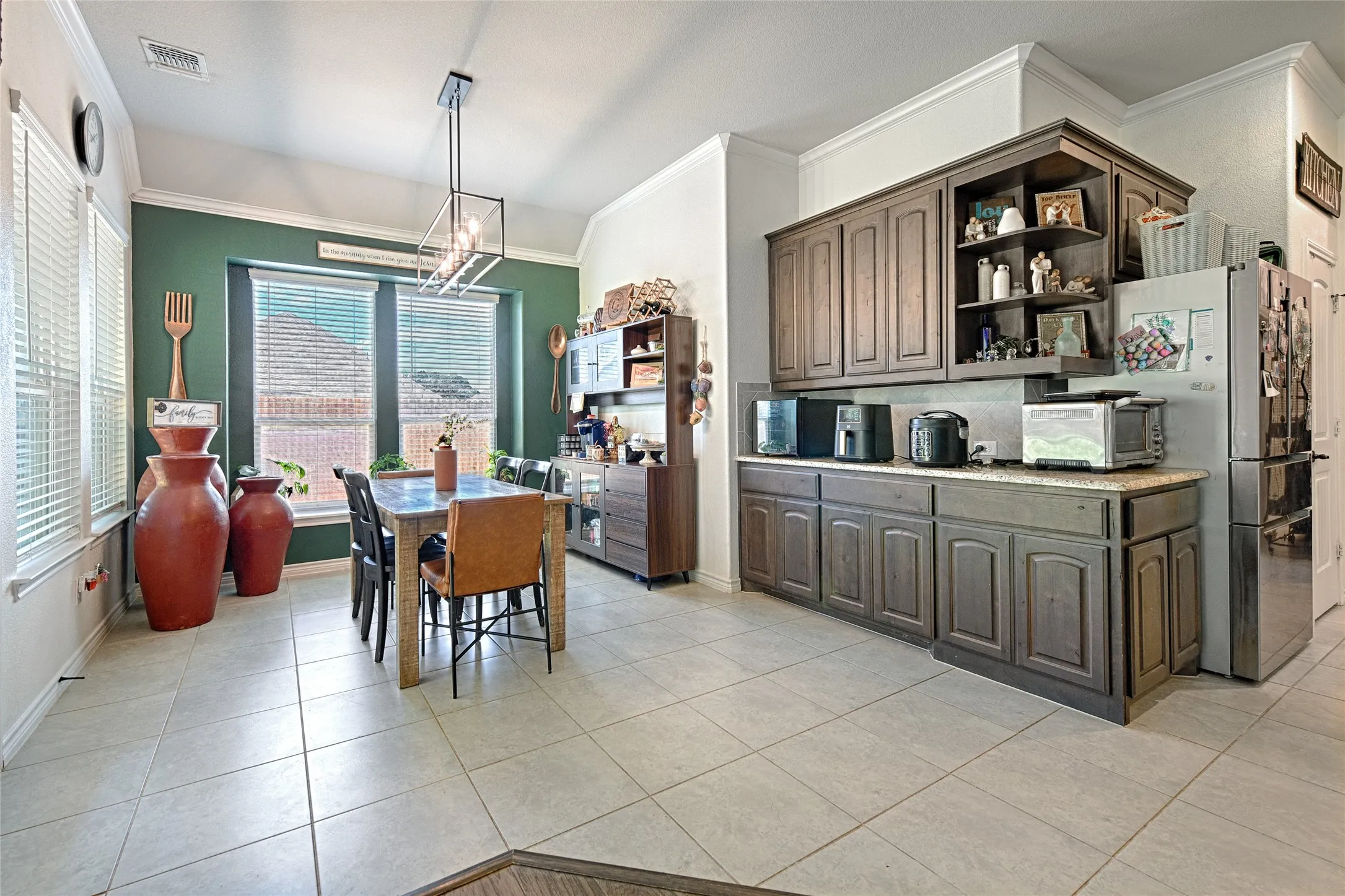 Kitchen featuring hanging light fixtures, ornamental molding, dark brown cabinets, and light tile floors