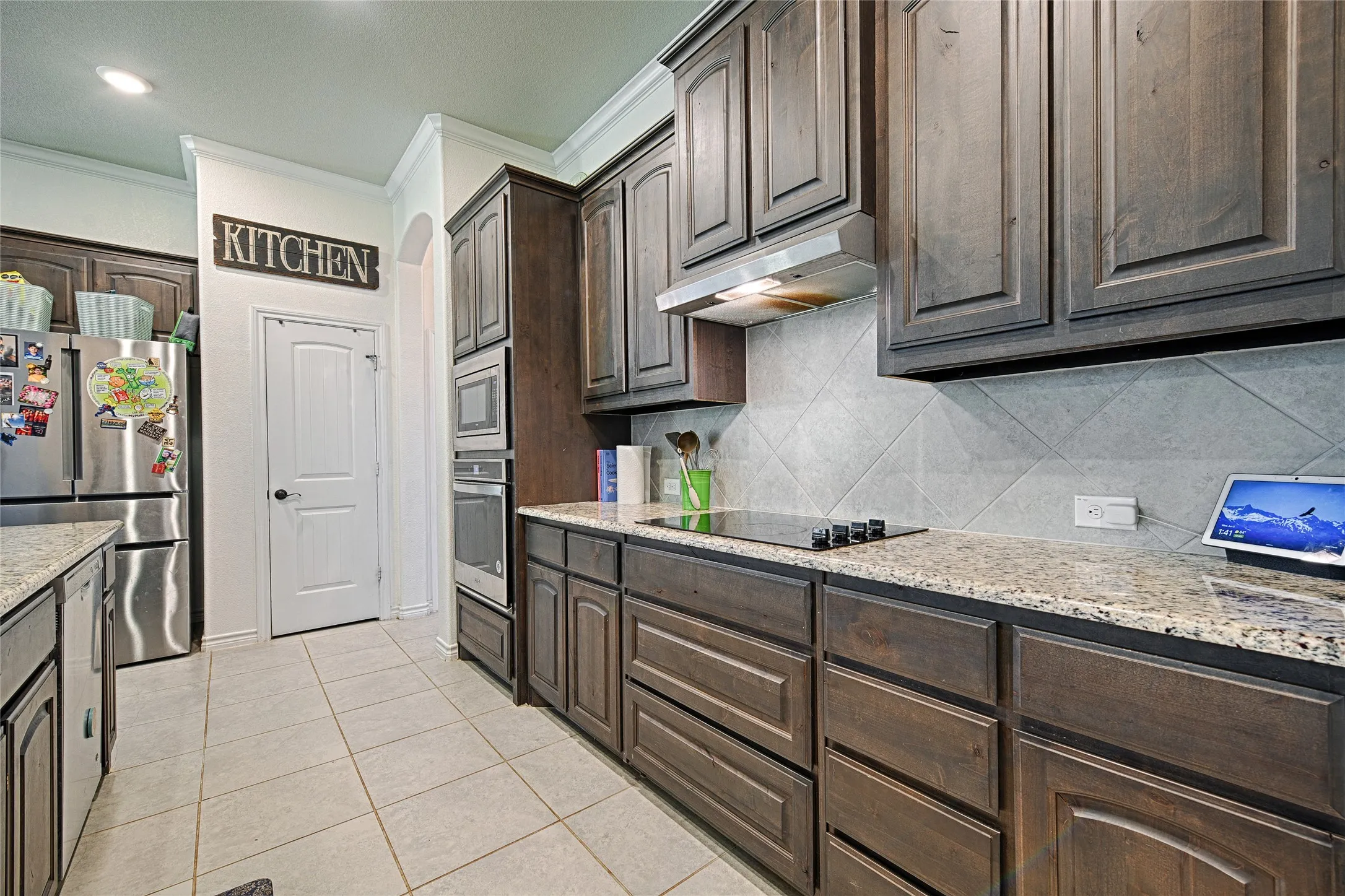 Kitchen featuring crown molding, light stone countertops, stainless steel appliances, backsplash, and dark brown cabinetry