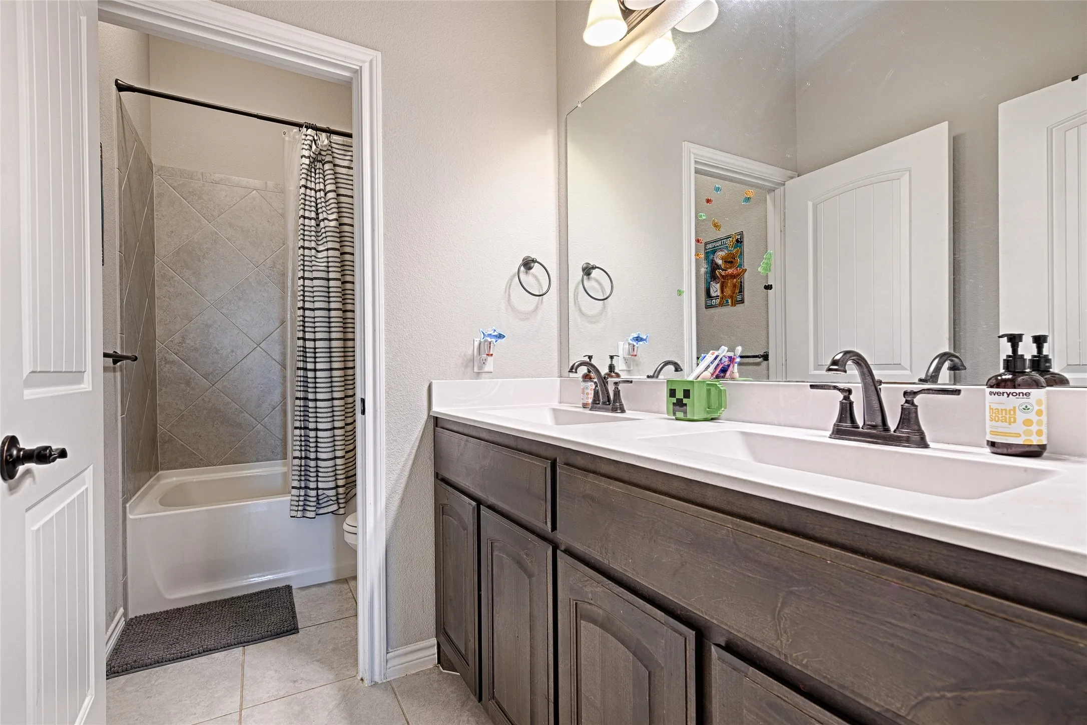 Full bathroom featuring tile floors, shower / bath combo with shower curtain, toilet, and dual bowl vanity