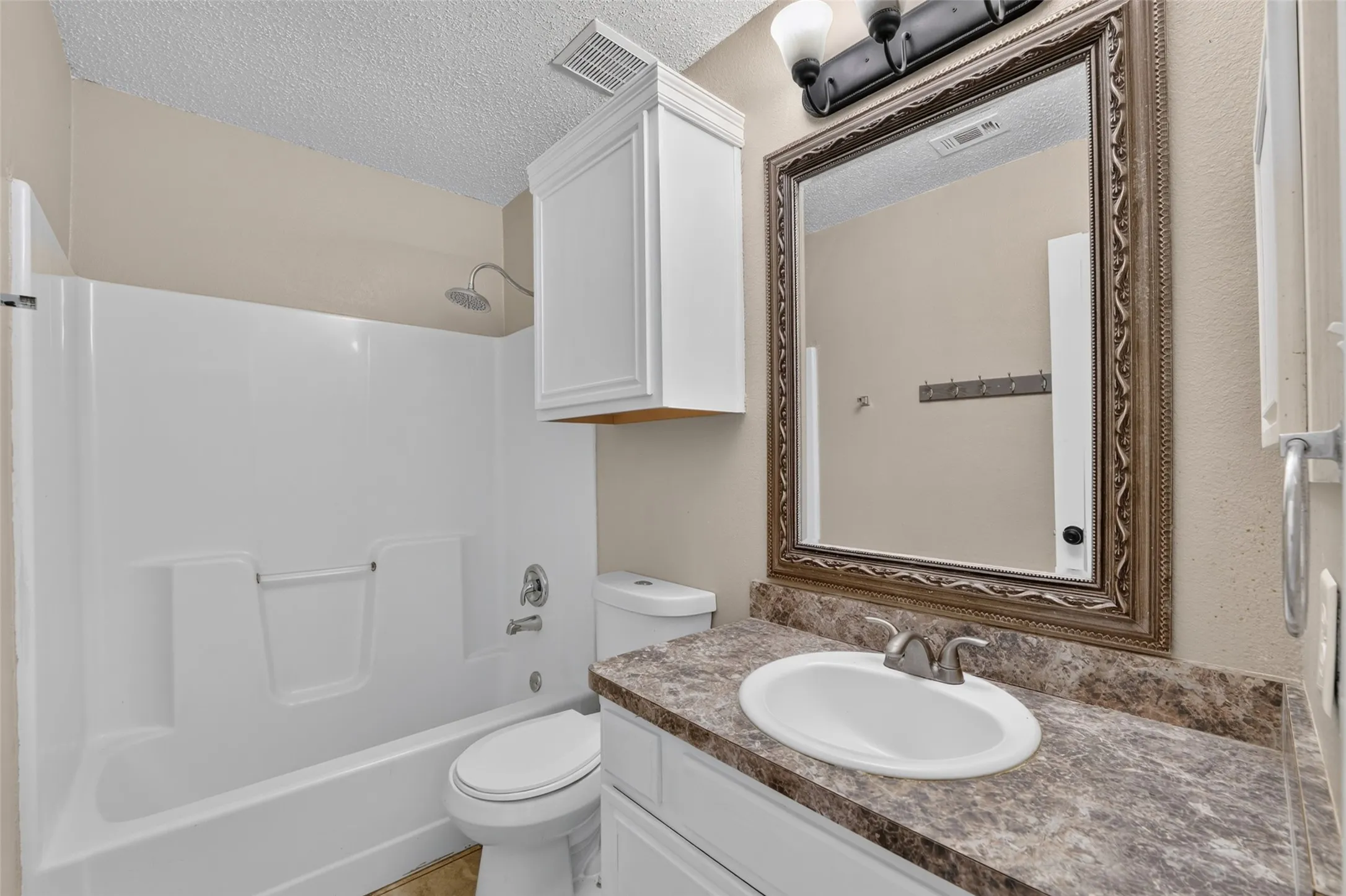 Bathroom with a white integrated shower/tub, a vanity featuring a patterned countertop, a white oval sink, and a framed mirror