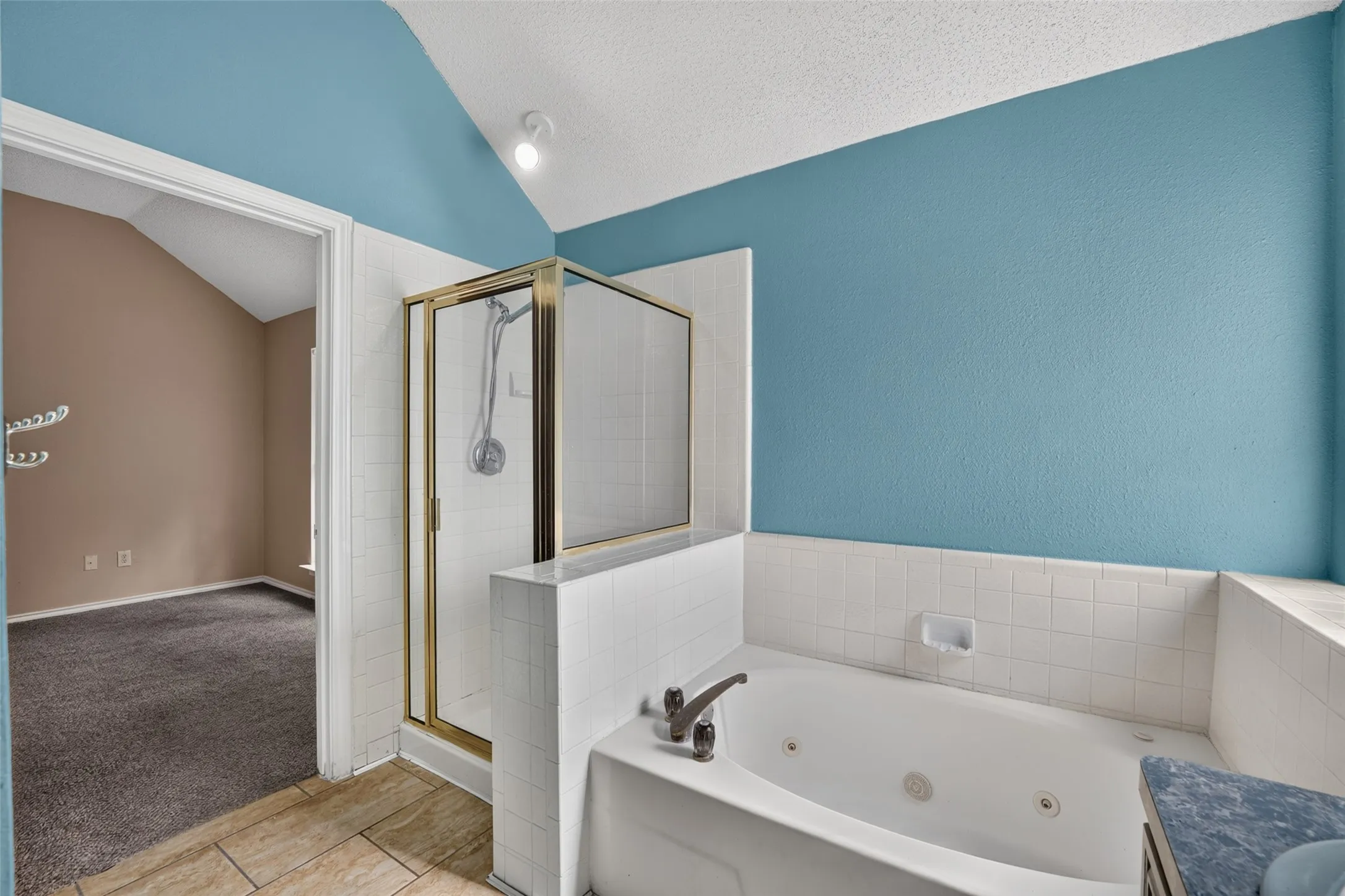 Spa tub with integrated jets, a separate glass-enclosed shower, white tile surround, and vaulted ceiling