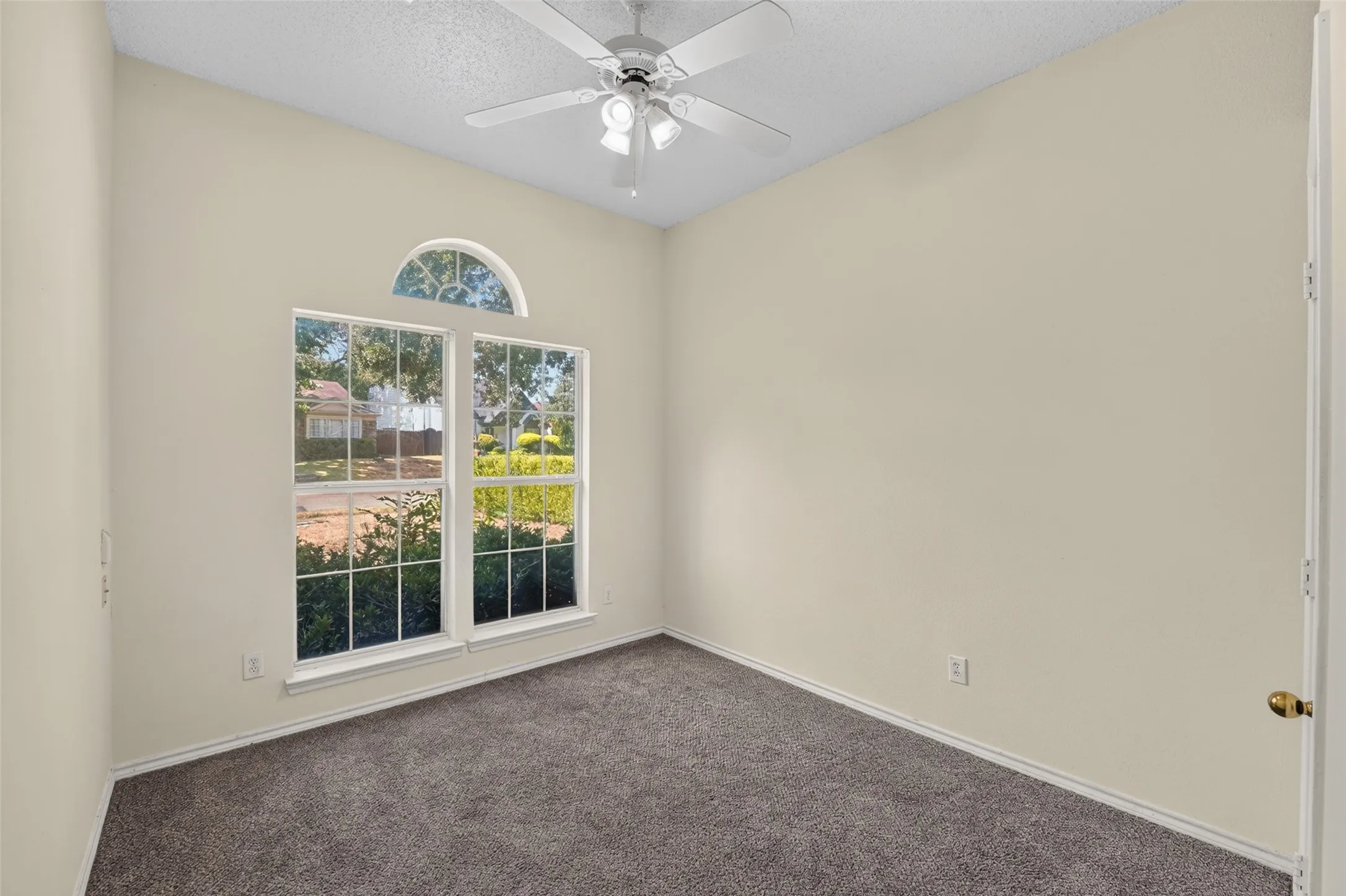 Carpeted room featuring a vaulted ceiling, a white ceiling fan with integrated lighting, and a multi-pane window with an arched transom