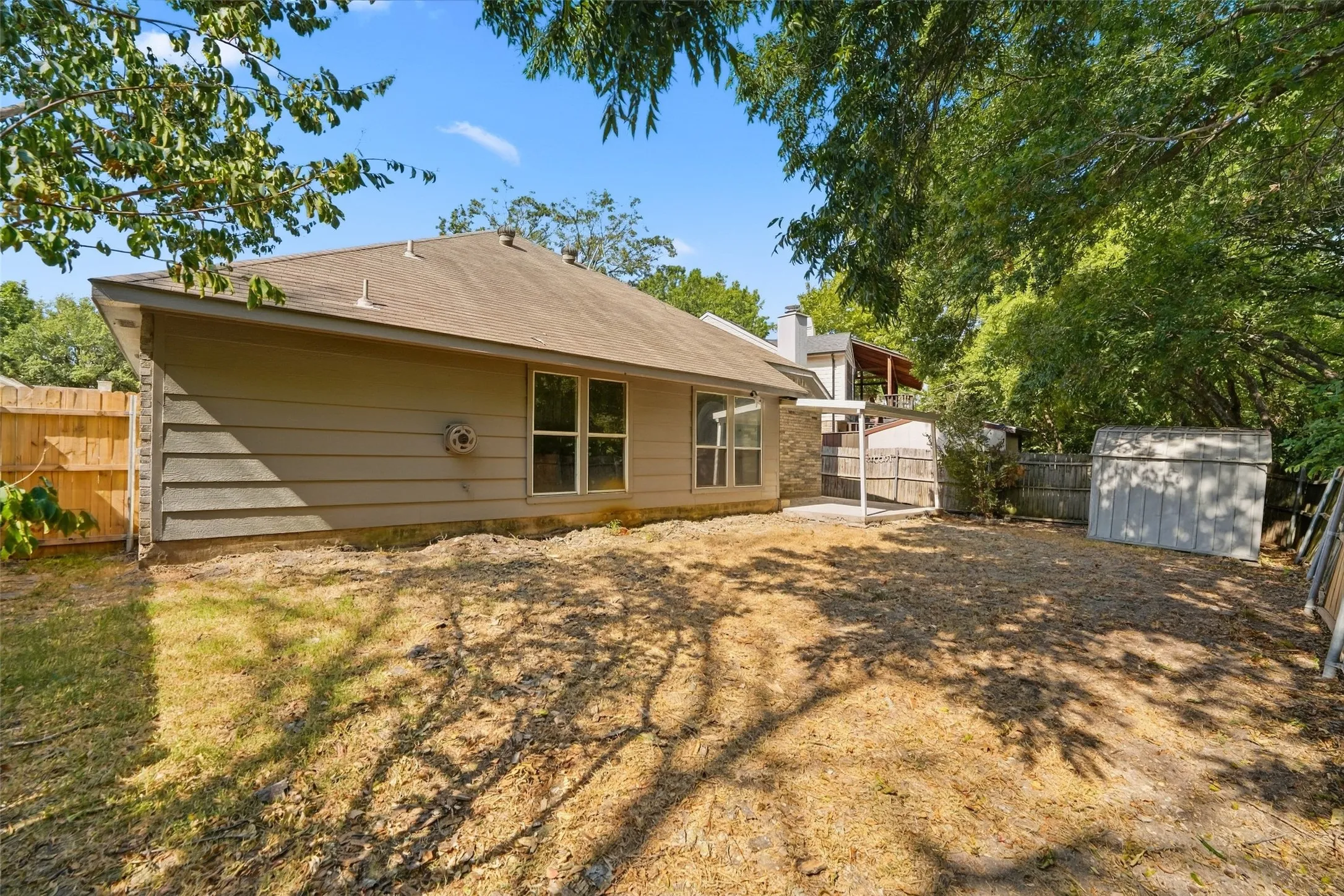 Expansive backyard with a covered patio, wood fencing, and a storage shed