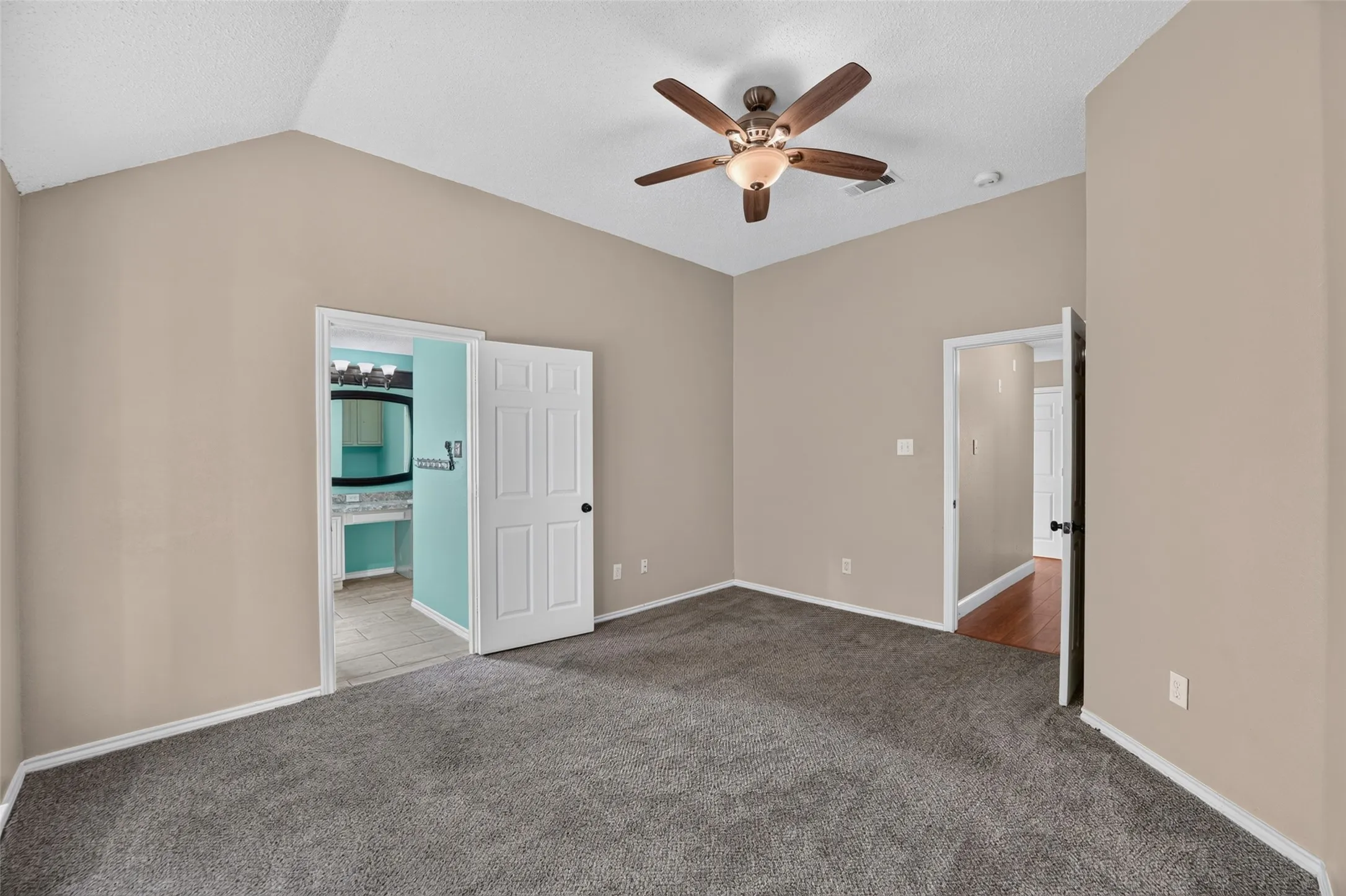 Vaulted ceiling, ceiling fan with light fixture, neutral wall color, gray carpet flooring, and a six-panel interior door
