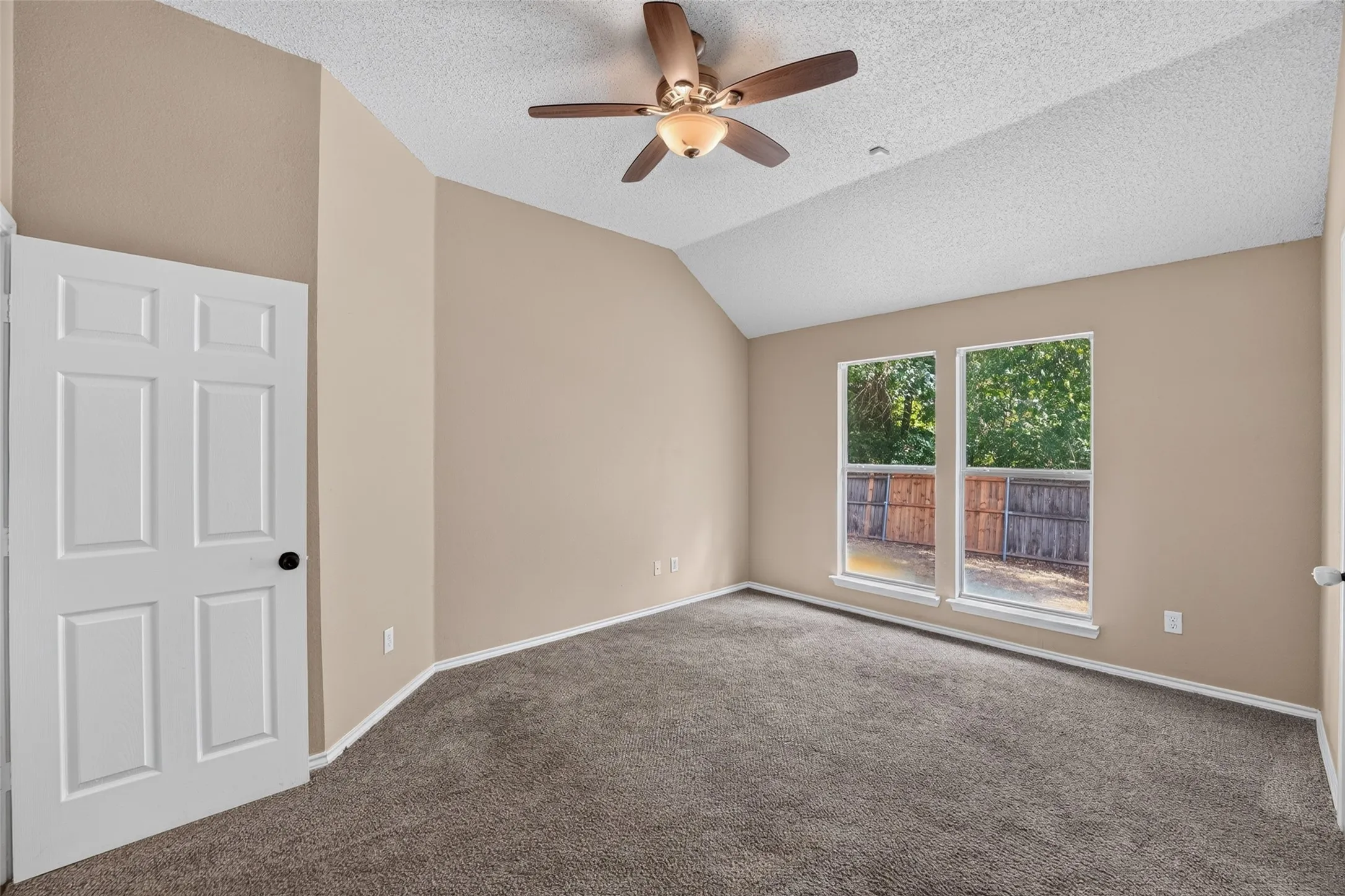 Vaulted ceiling with a ceiling fan, dual windows, plush carpeting, and a six-panel door