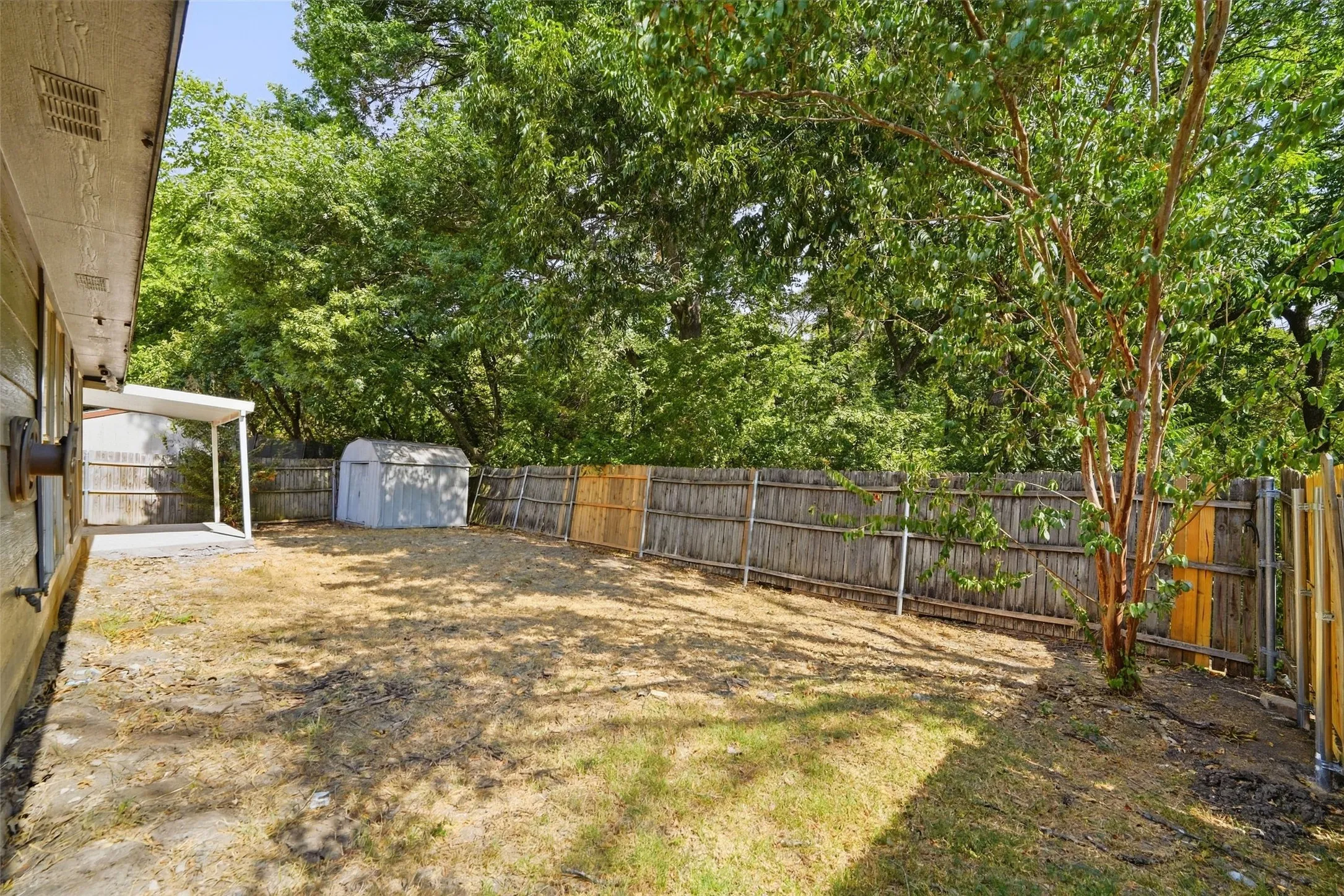 Expansive backyard with mature trees, privacy fencing, and a covered patio area