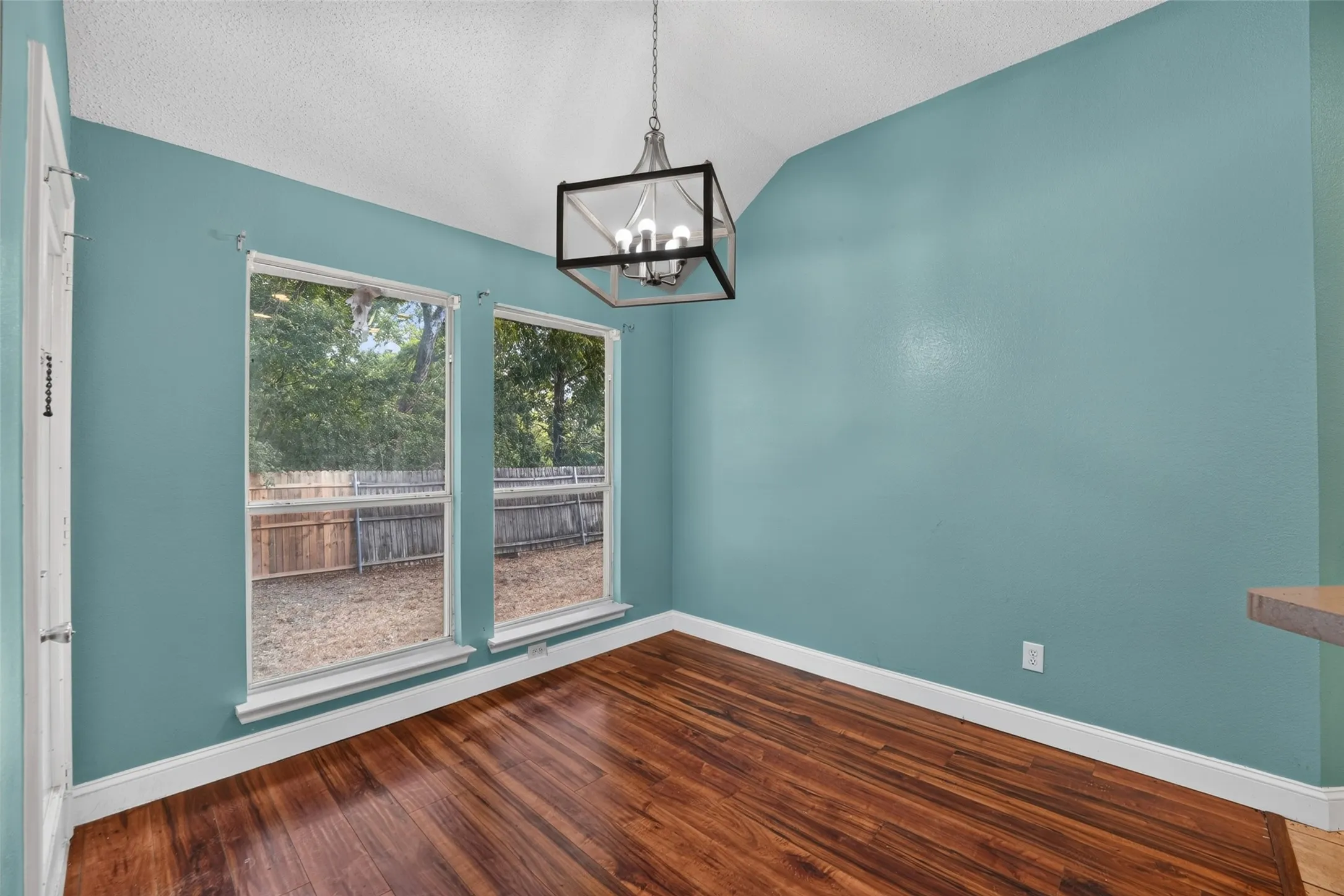 Angled ceiling with a contemporary chandelier, wood-finish flooring, and two windows