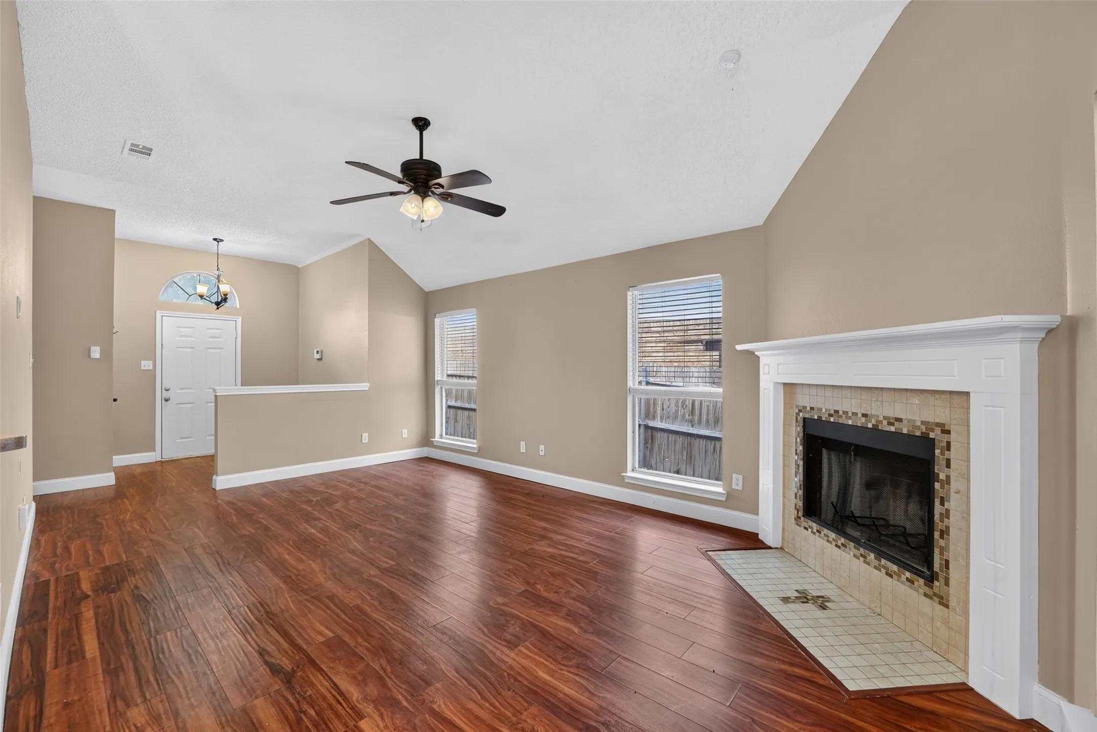 Vaulted ceiling with a ceiling fan, wood-finish flooring, fireplace with a tile surround and mantel, and multiple windows
