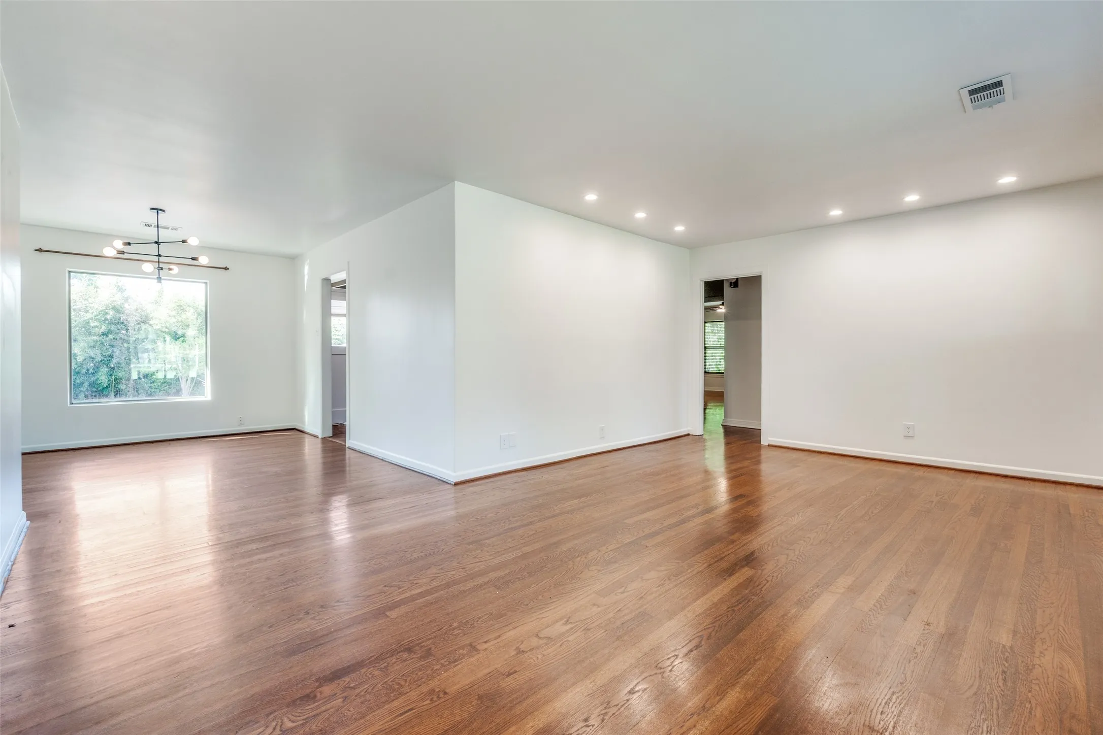 Empty room featuring a notable chandelier, wood finished floors, baseboards, visible vents, and recessed lighting
