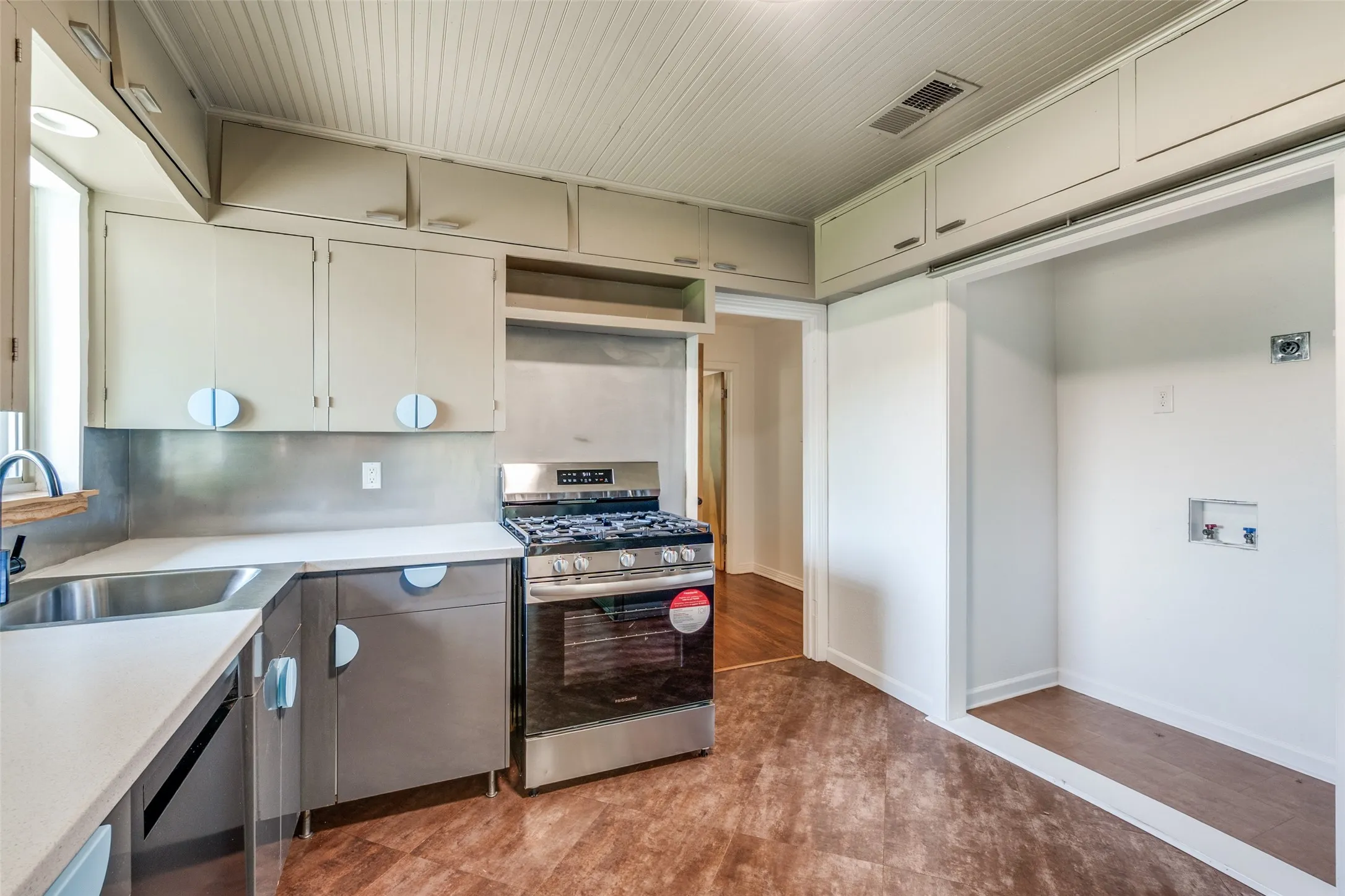 Kitchen featuring light countertops, range hood, a sink, visible vents, and appliances with stainless steel finishes
