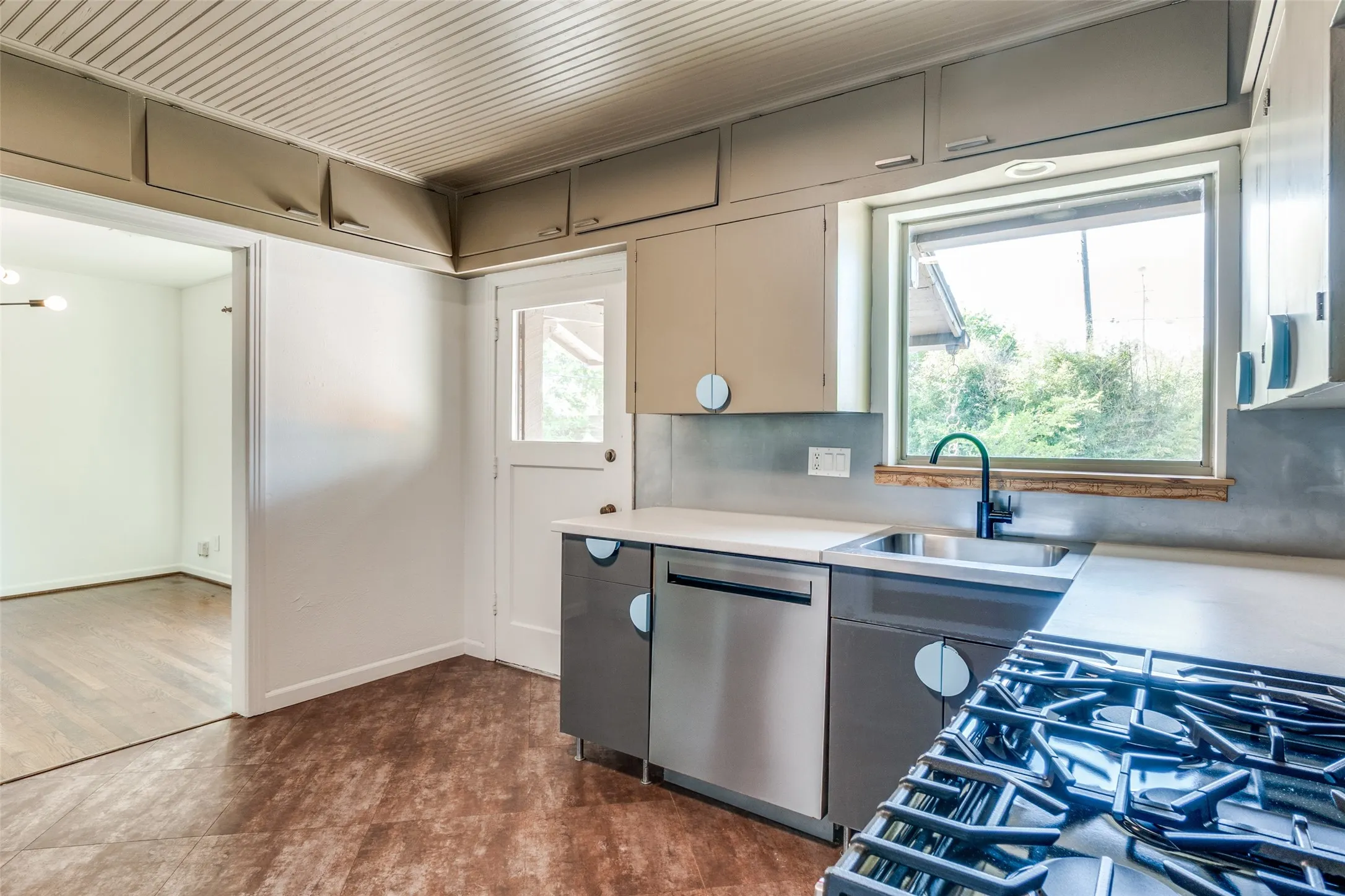 Kitchen with light countertops, dishwasher, baseboards, dark wood-type flooring, and a sink