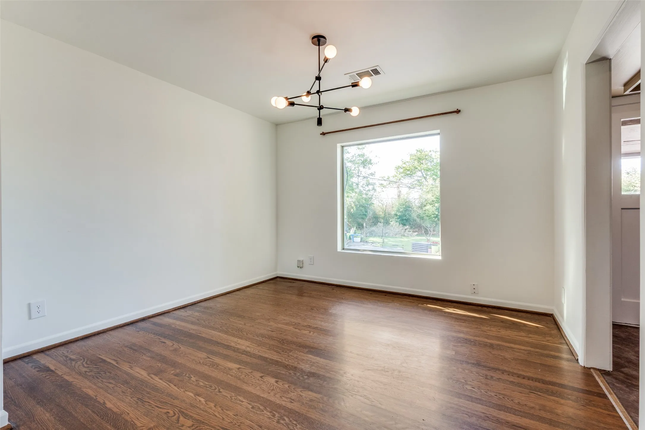 Spare room with baseboards, visible vents, dark wood-style flooring, and an inviting chandelier