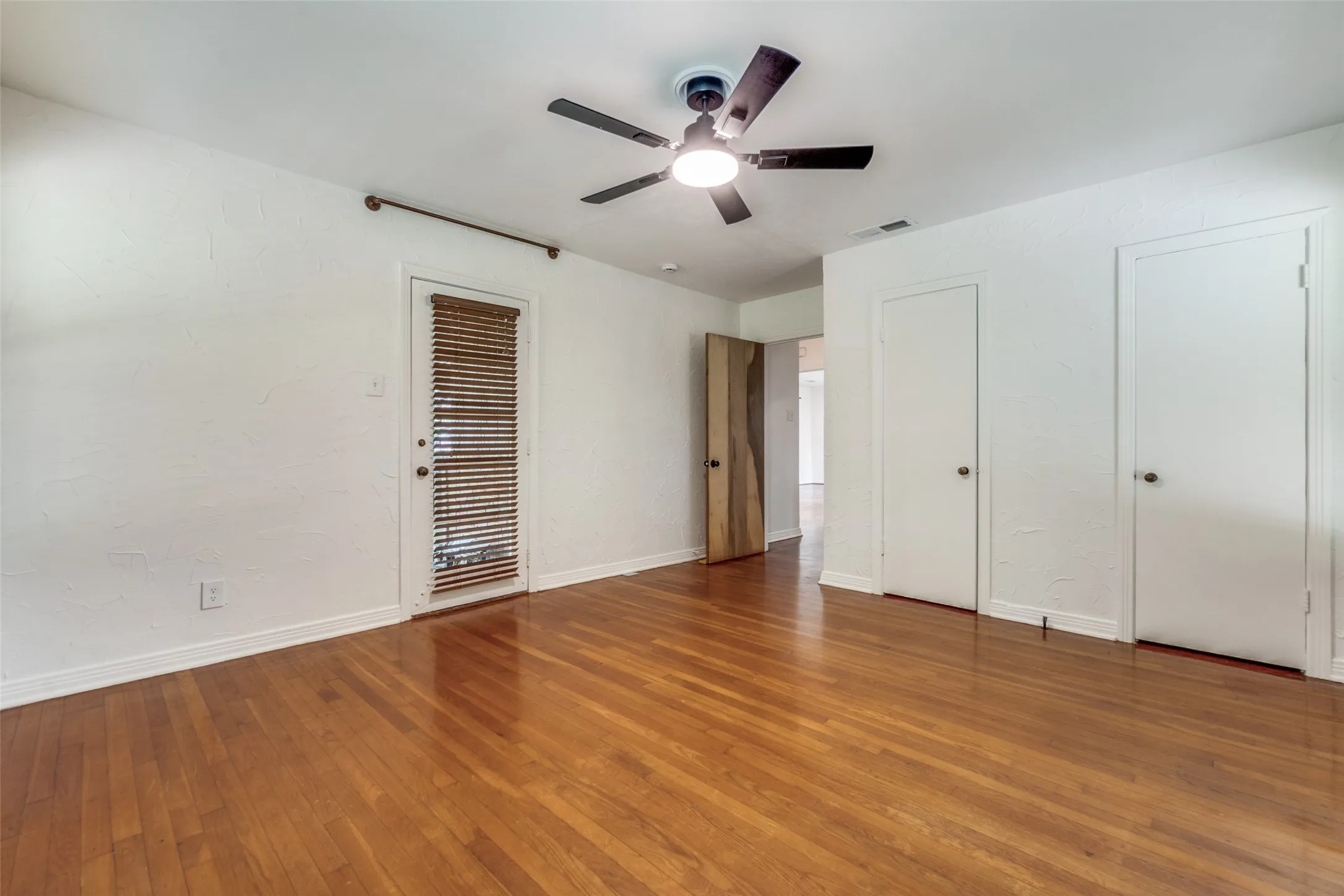 Unfurnished bedroom with two closets, baseboards, hardwood / wood-style flooring, ceiling fan, and visible vents