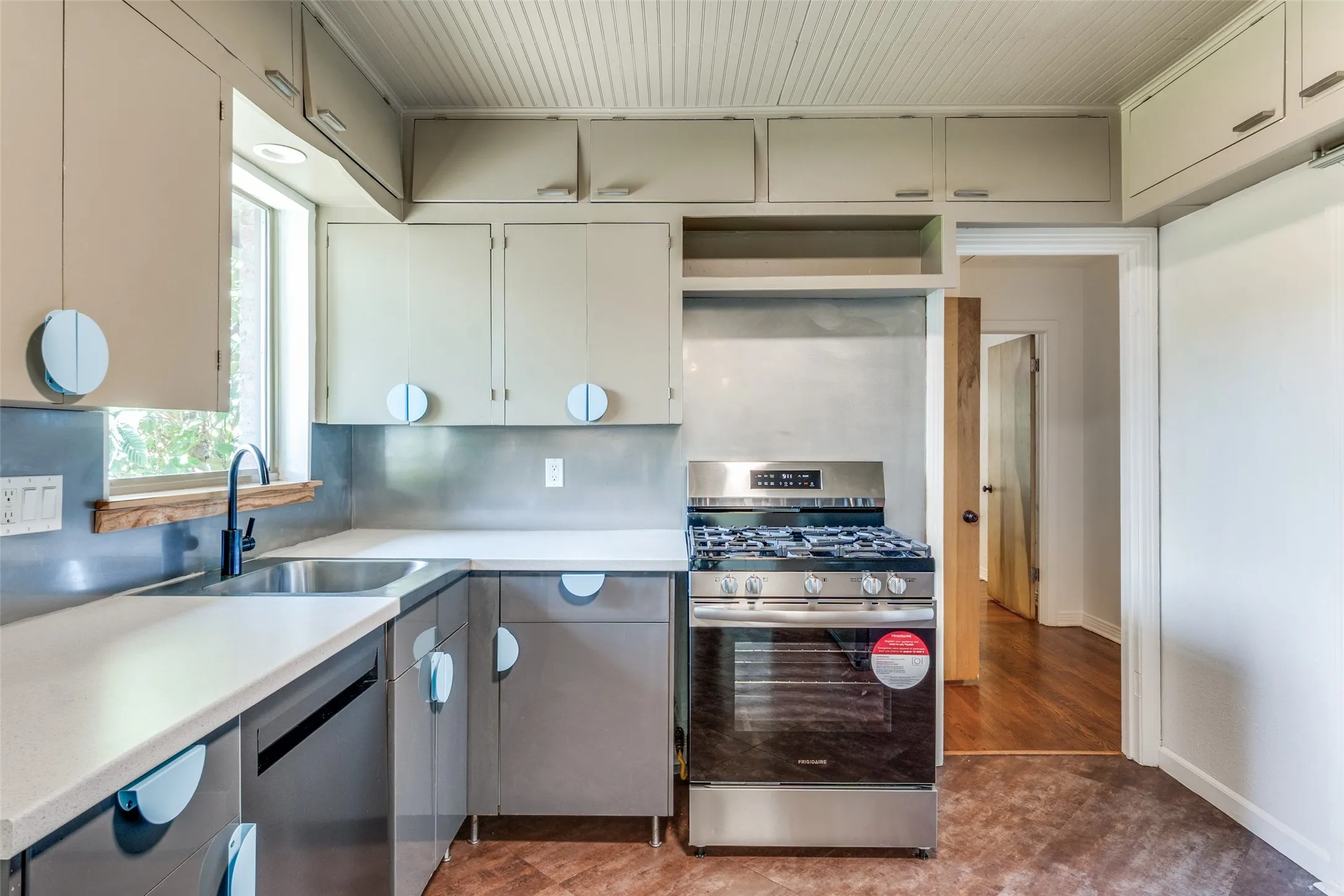 Kitchen featuring decorative backsplash, light countertops, baseboards, stainless steel appliances, and a sink