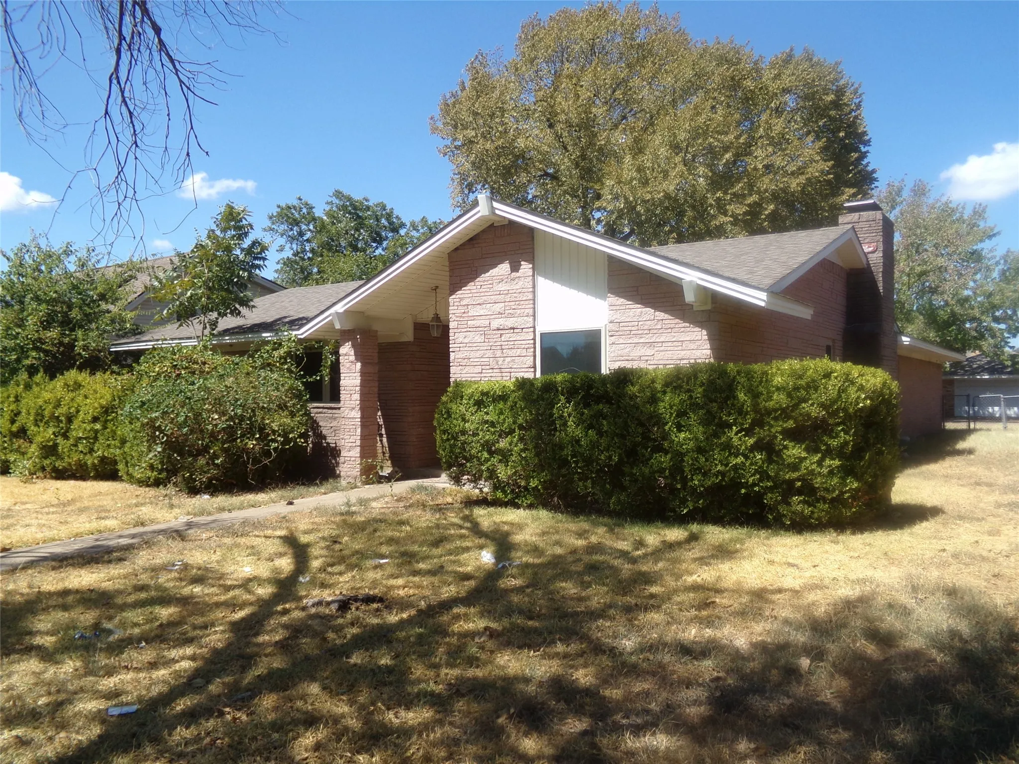 Brick exterior with a gabled roofline, front entryway, prominent chimney, and established shrubbery