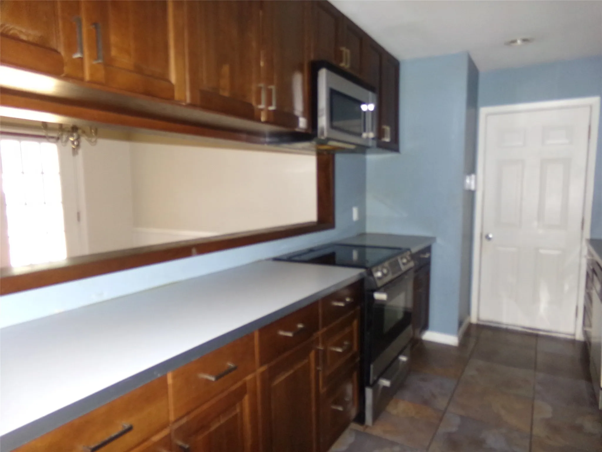 Wood-finish cabinetry with modern hardware, integrated stainless steel microwave, black electric range, and stone tile flooring