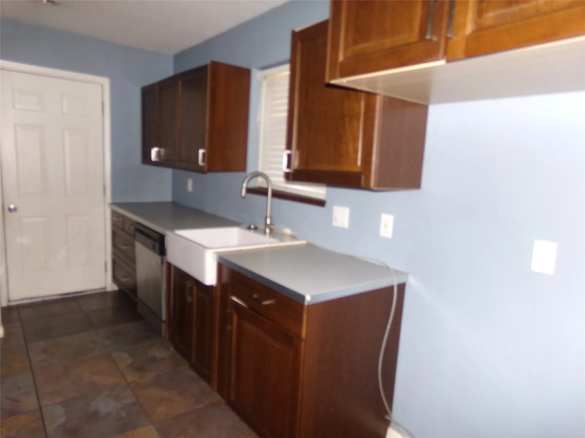 Rich wood cabinetry, an apron-front sink, stainless steel dishwasher, and tiled flooring