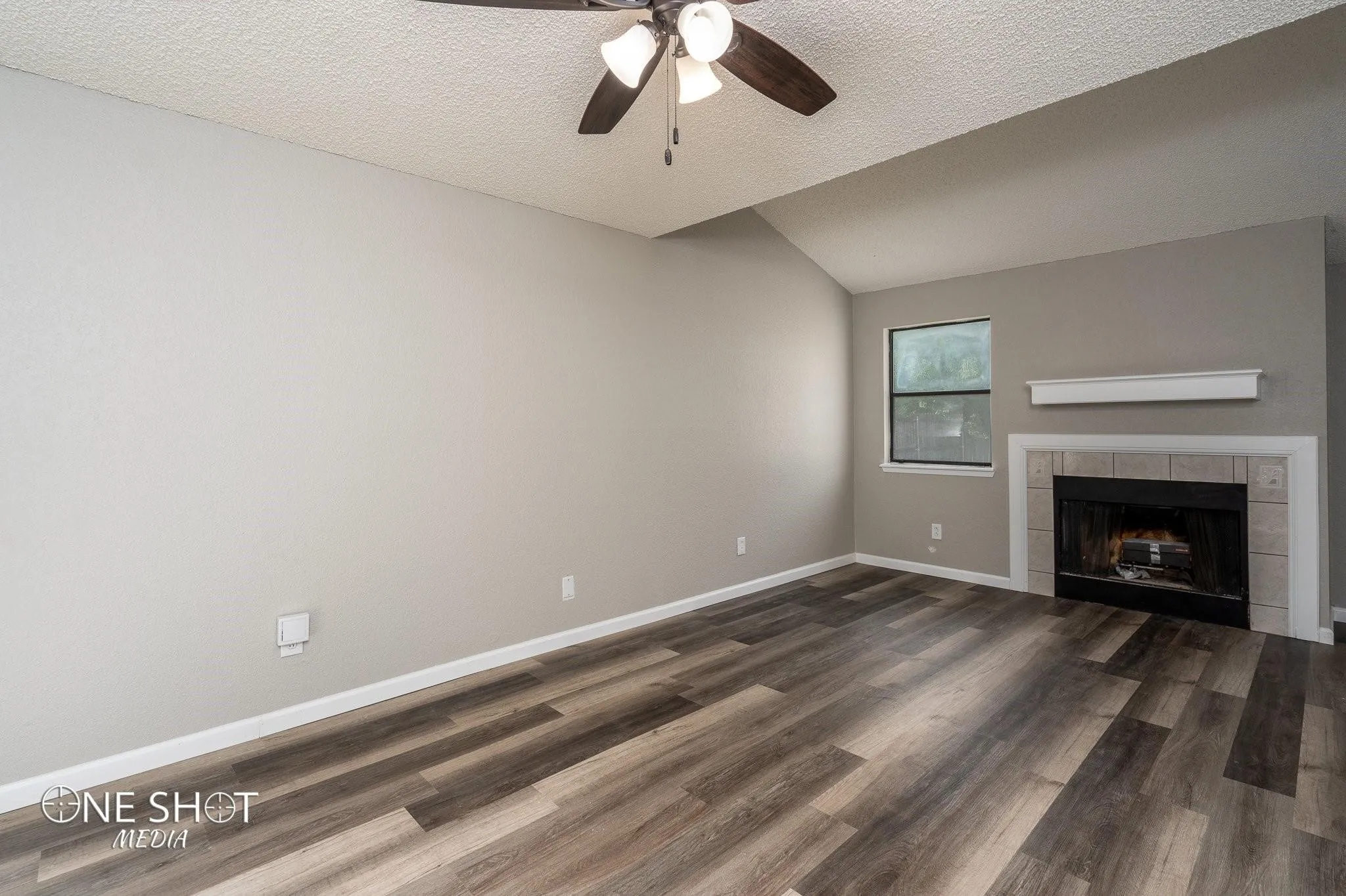 Unfurnished living room featuring ceiling fan, hardwood / wood-style flooring, a tile fireplace, and a textured ceiling