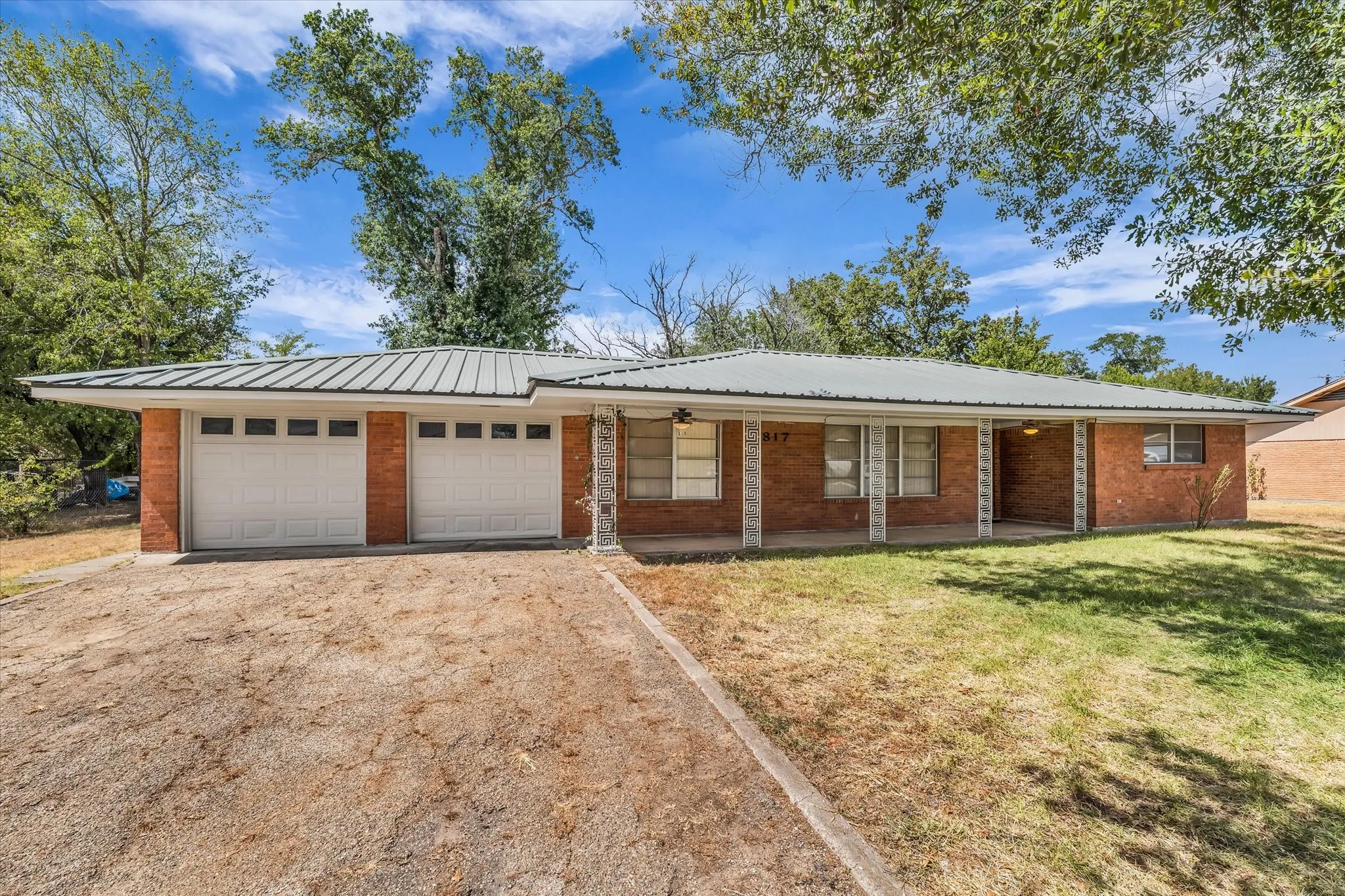 Front View of 817 Holly Lane, featuring a brick exterior, metal roof, 2 car garage, large covered porch, and paved driveway.