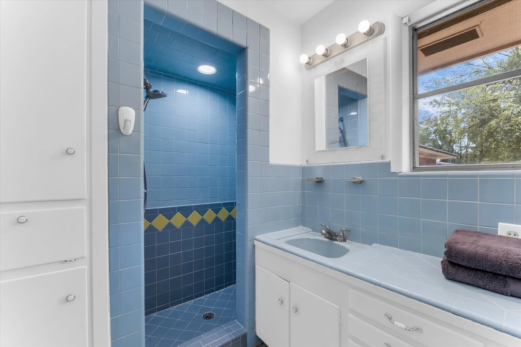 Primary bath features beautiful natural lighting, built-in storage, and charming original tile.