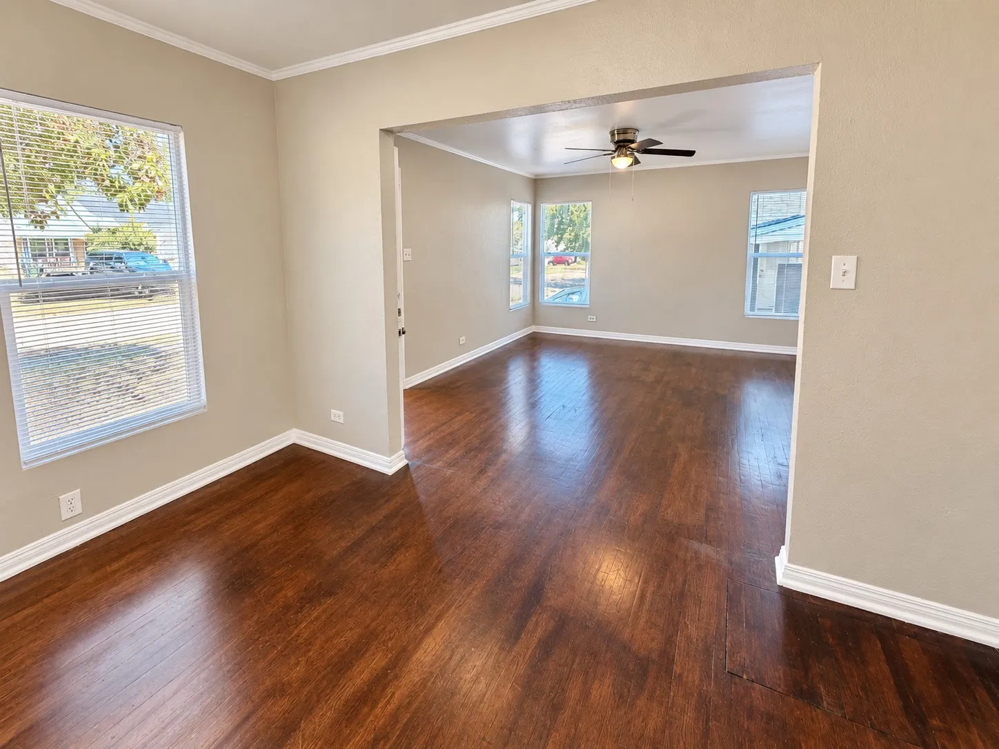 Expansive open floor plan featuring wood-finish flooring, multiple windows with blinds, and a ceiling fan in the adjacent space