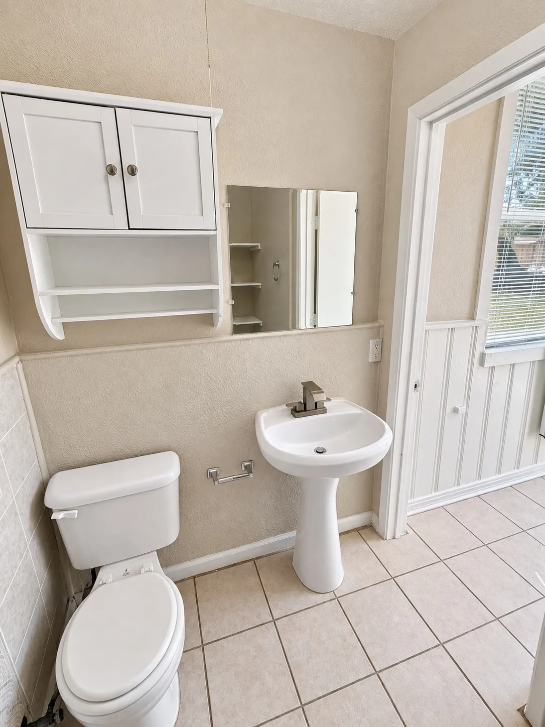 Pedestal sink with brushed nickel faucet, wall-mounted storage cabinet, mirrored medicine cabinet, ceramic tile flooring, and beadboard paneling