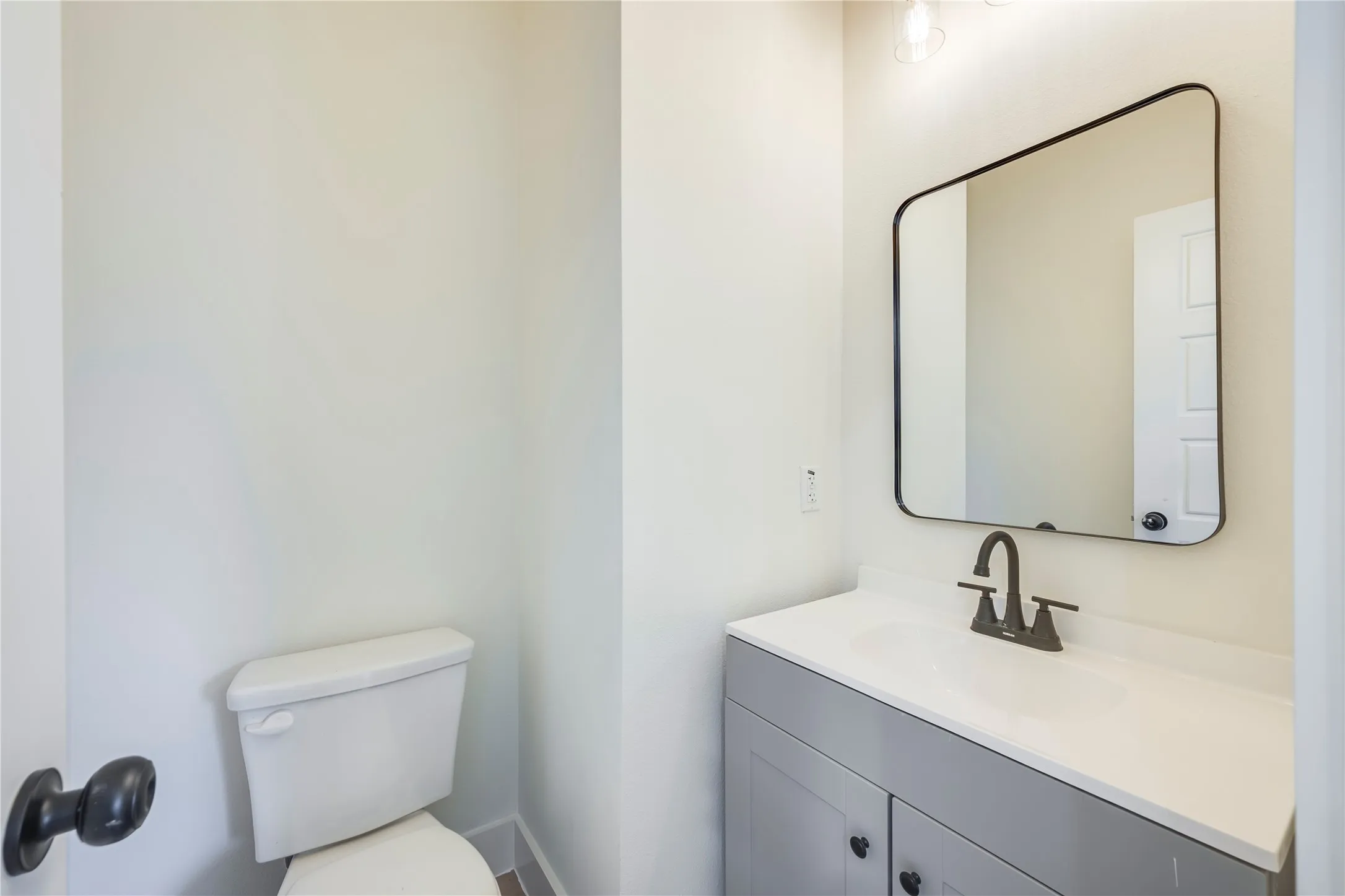 White vanity countertop with an integrated sink, framed mirror, two-door vanity cabinet, and matte black faucet