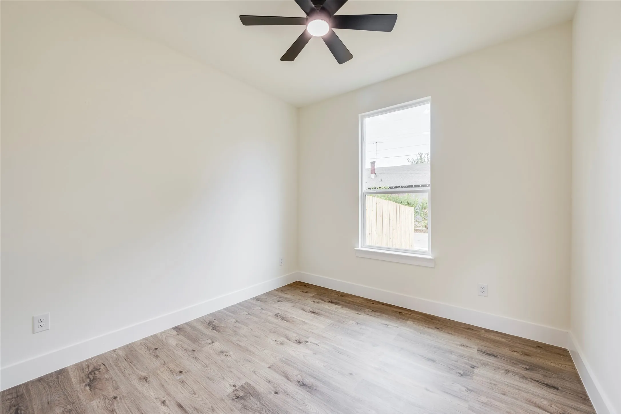 Wood-finish flooring, neutral wall tones, a single window, and a ceiling fan with integrated lighting
