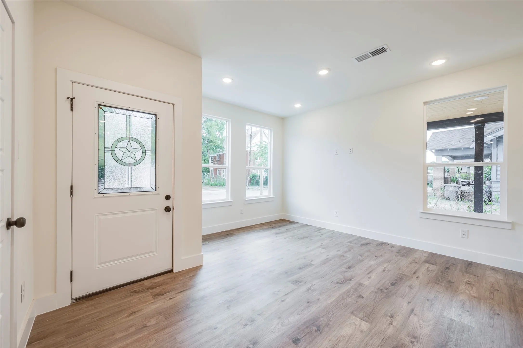 Entry door with decorative glass inlay, wood-finish flooring, white walls, recessed lighting, and multiple windows