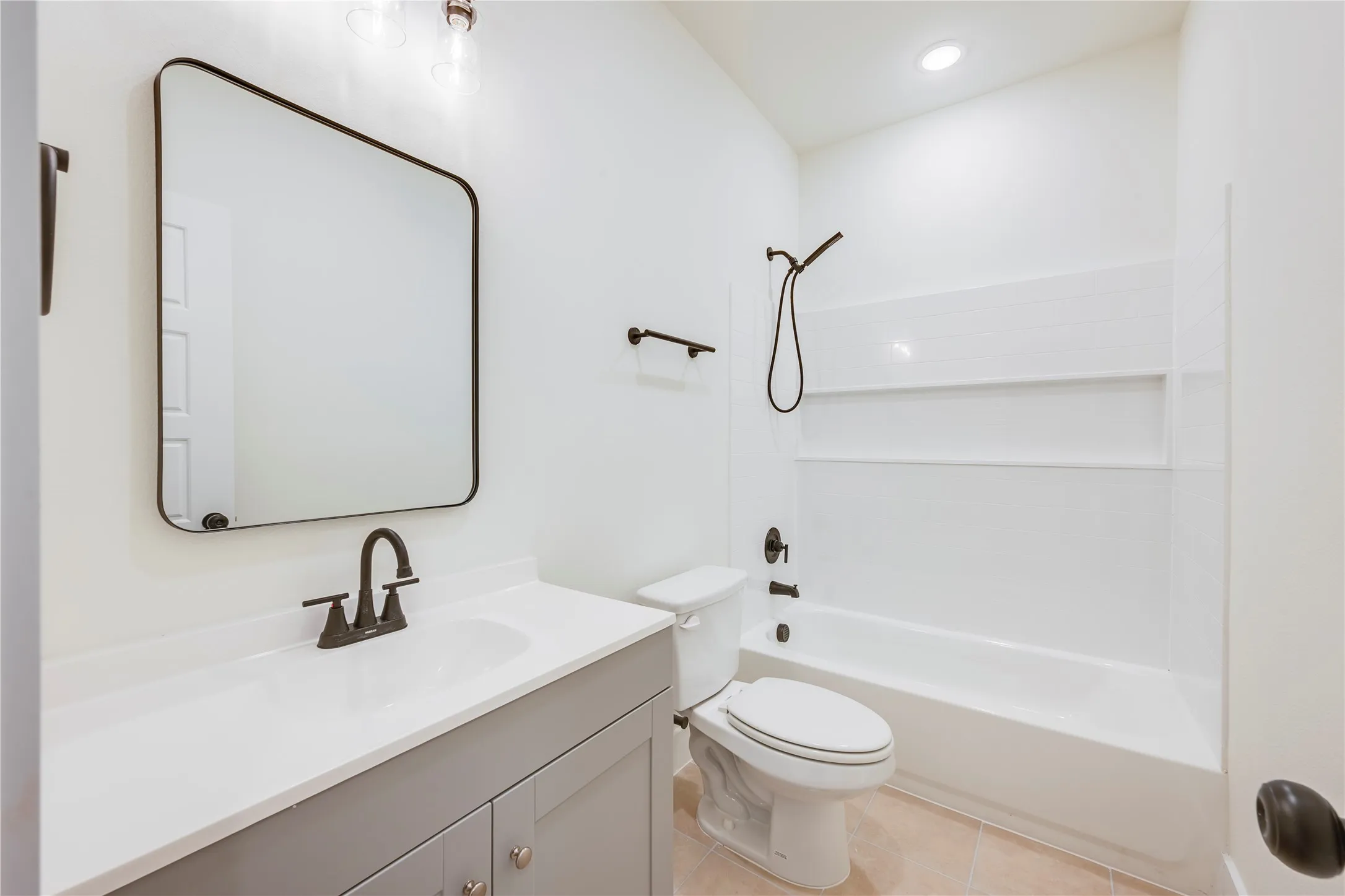Bathroom featuring a single vanity with a solid surface countertop, matte black fixtures, a framed mirror, and a tub-shower combination with integrated shelving