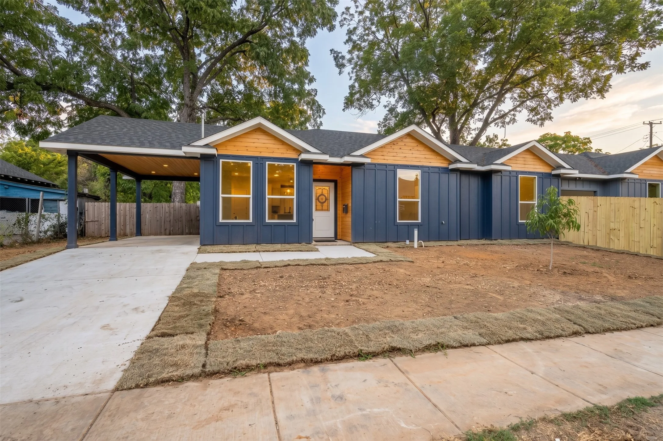 Contemporary exterior with dark blue siding, light wood-tone gables, a covered carport, and a concrete driveway