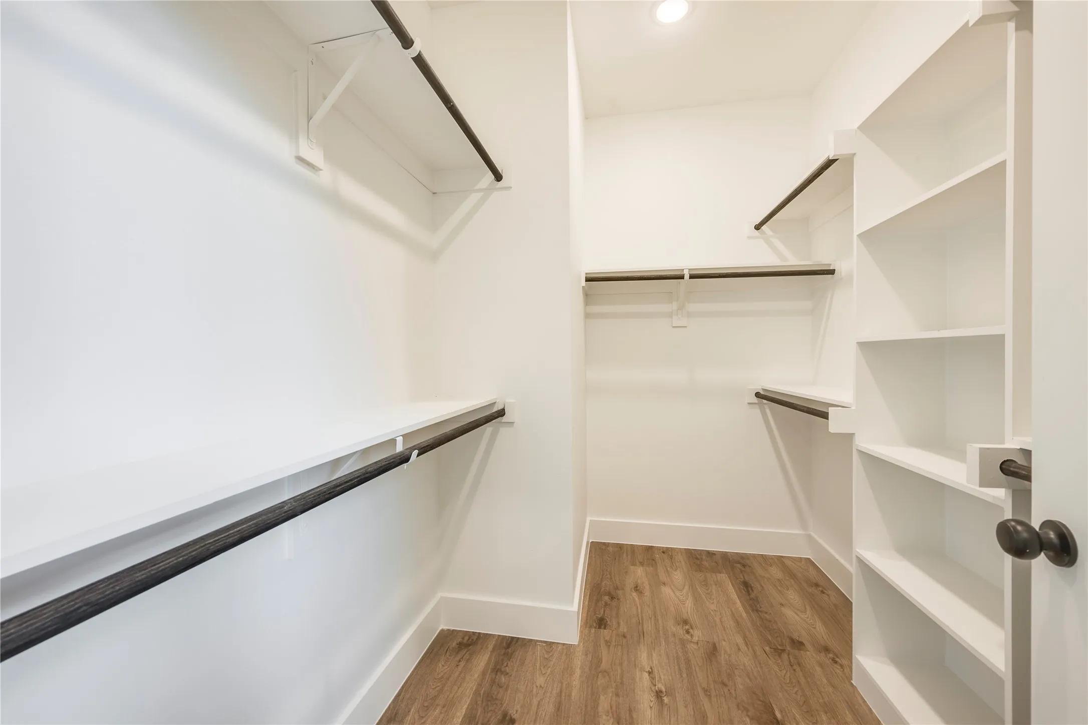 Walk-in closet with wood-finish flooring, extensive built-in shelving, multiple hanging rods, and recessed lighting